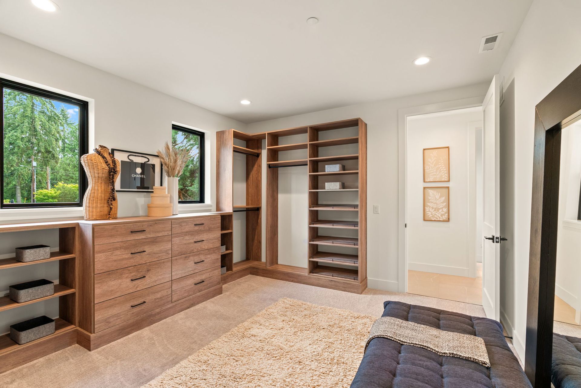 Modern and roomy bedroom closet with built-in wooden shelves, dresser, large windows, and neutral decor
