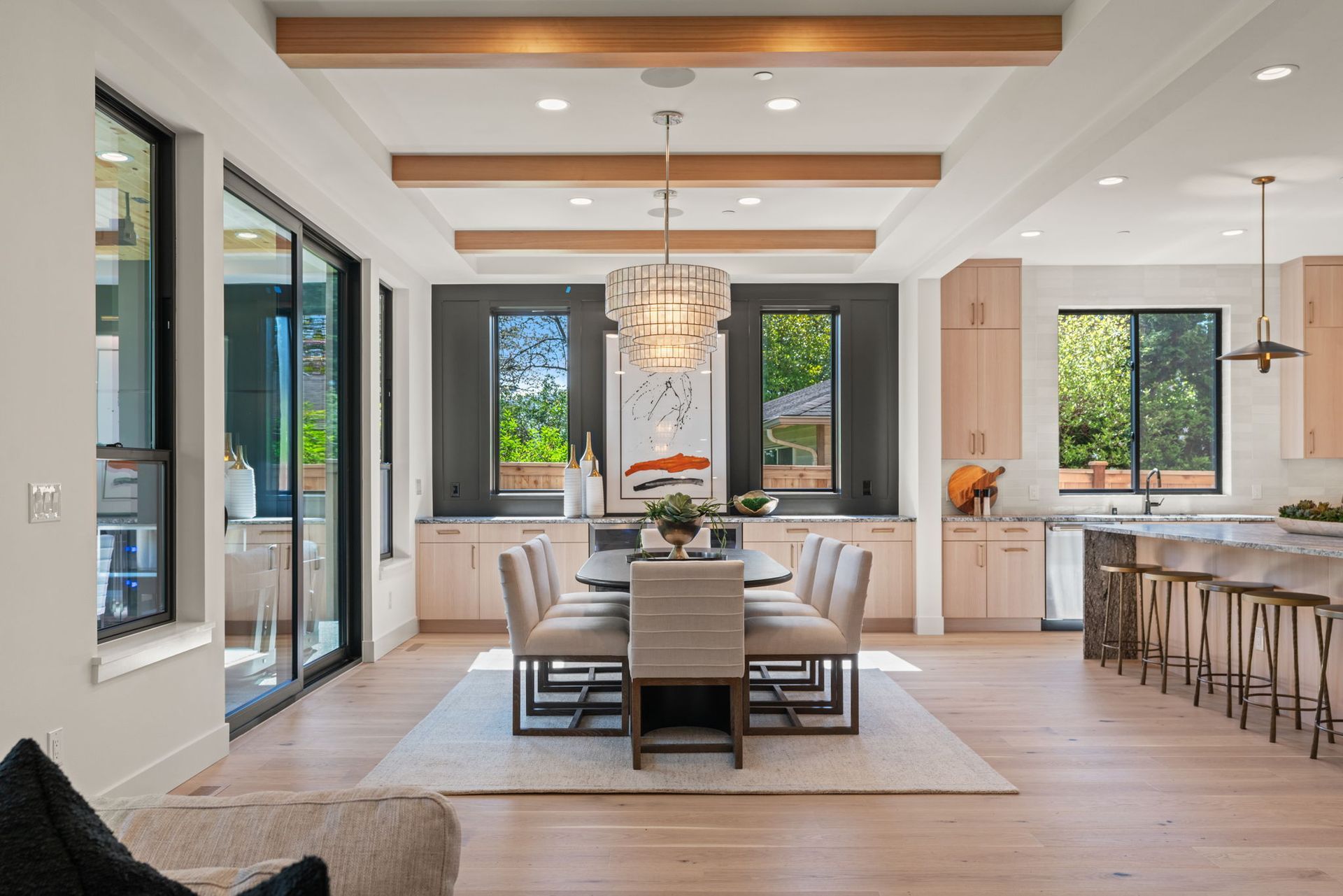 Bright modern open-concept living and dining room with wood beams, chandelier, and kitchen island bar stools