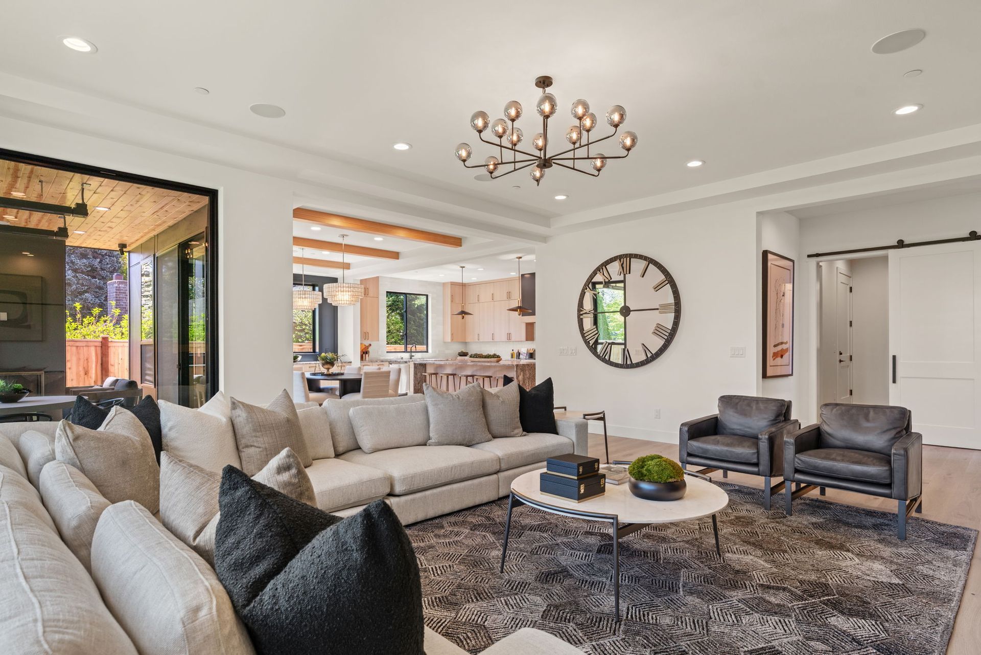 Bright modern living room with beige sofas, gray chairs, large wall clock, and chandelier