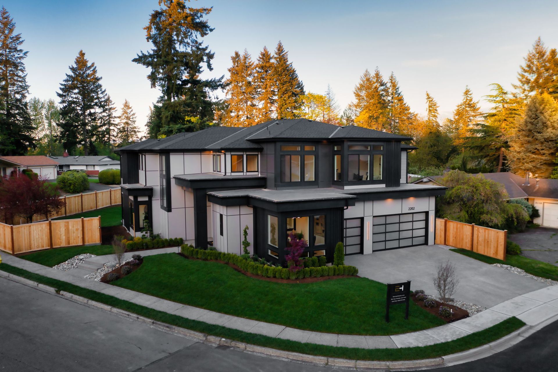 Modern two-story house with gray exterior, garage, curved driveway, and trees at sunset
