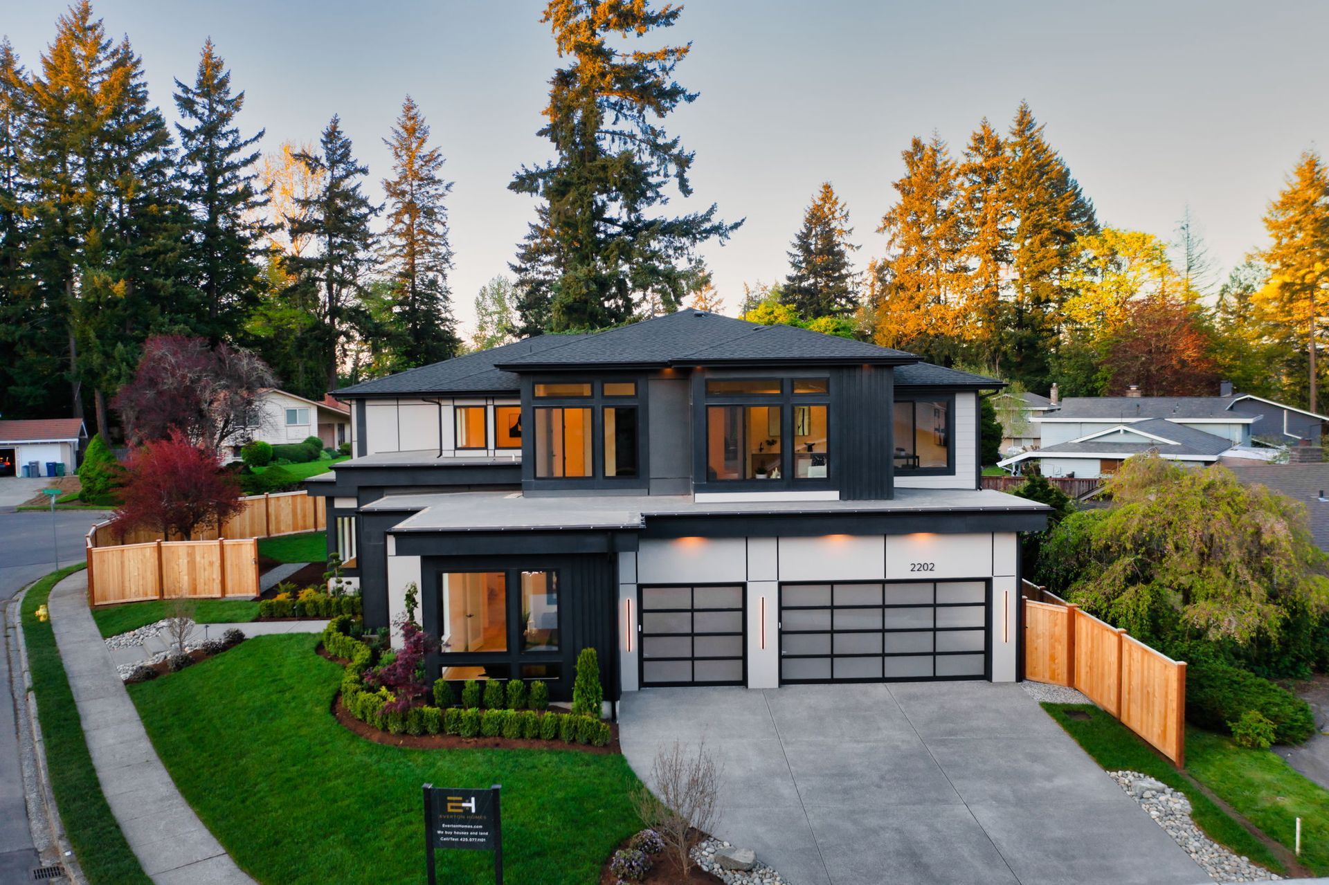 Modern two-story house with gray exterior, double garage, and landscaped yard at sunset
