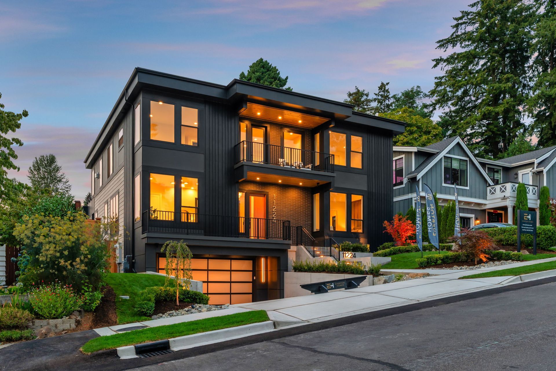 Modern dark-gray house with warm lights at dusk on a tree-lined street