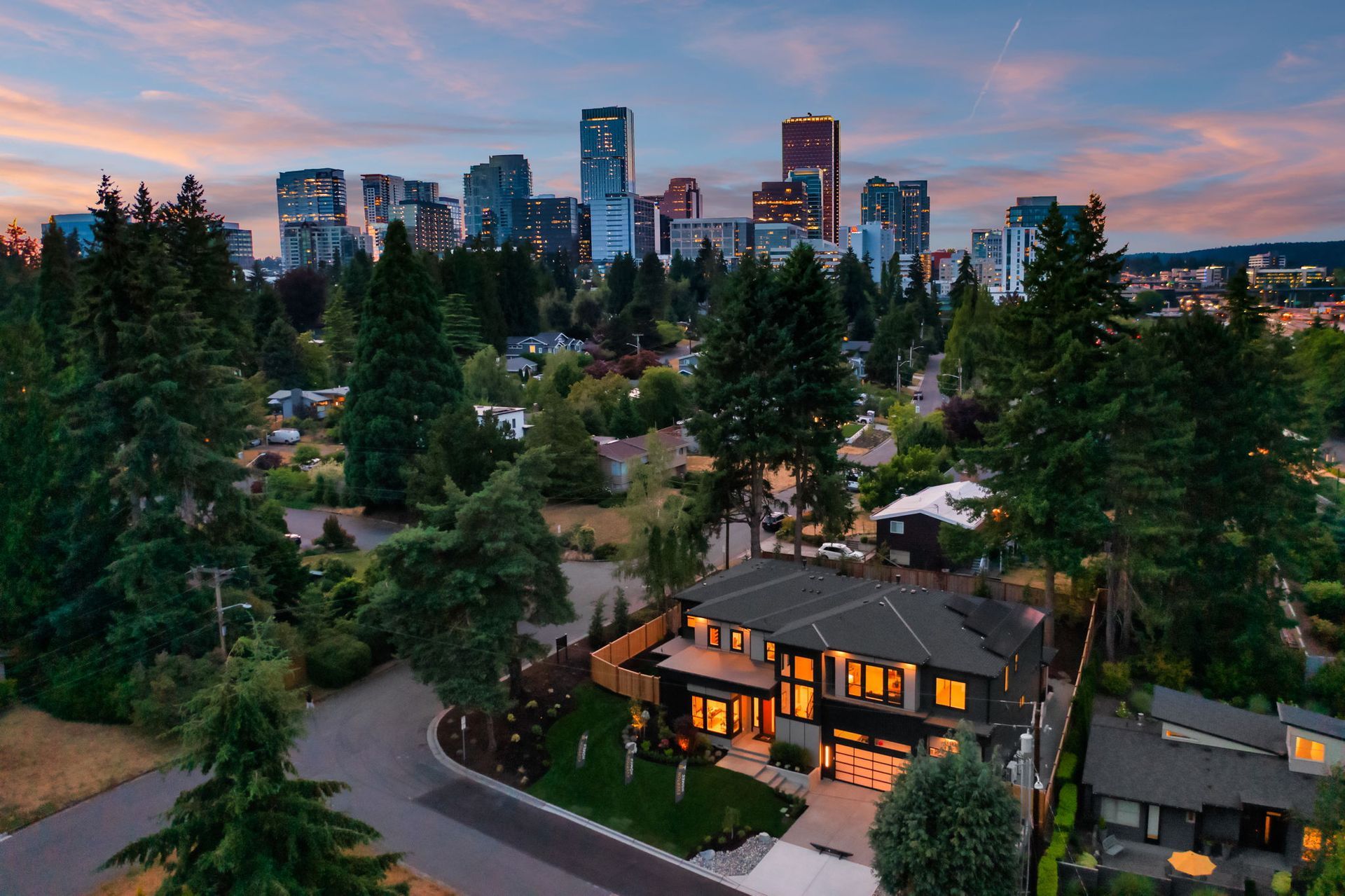 Dusk skyline above a tree-lined neighborhood, with a warmly lit house in the foreground.
