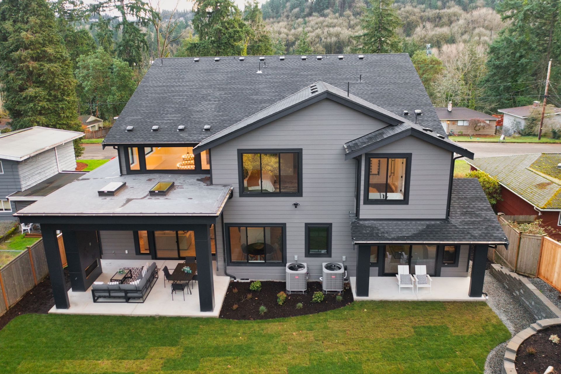 Gray two-story house with black trim, patio, and dark gray roof. Surrounded by a green lawn and trees.