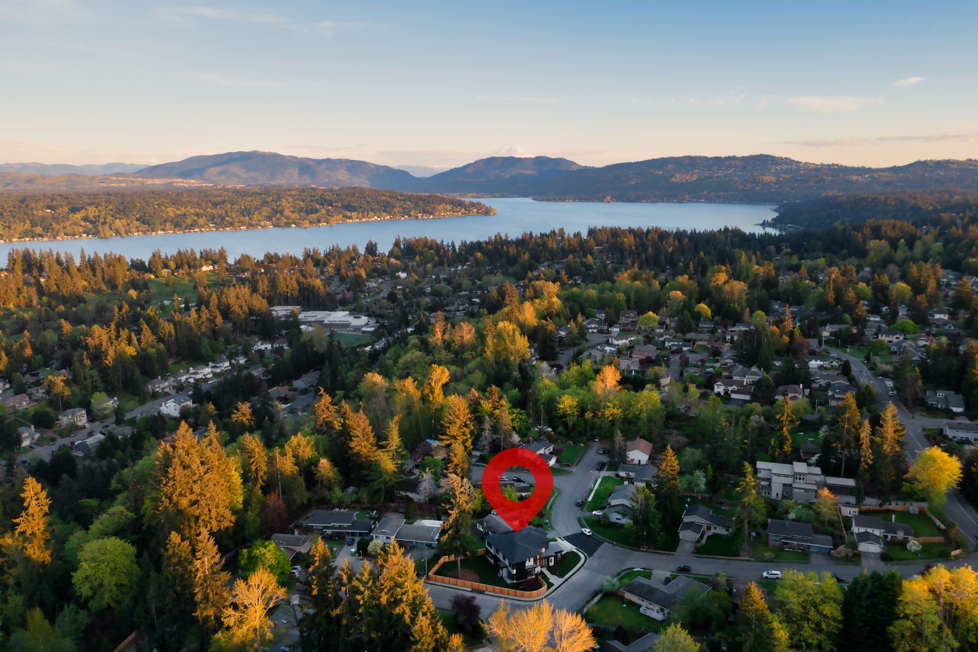 Aerial view of a leafy suburban neighborhood by a lake at sunset, with a red map pin marker.