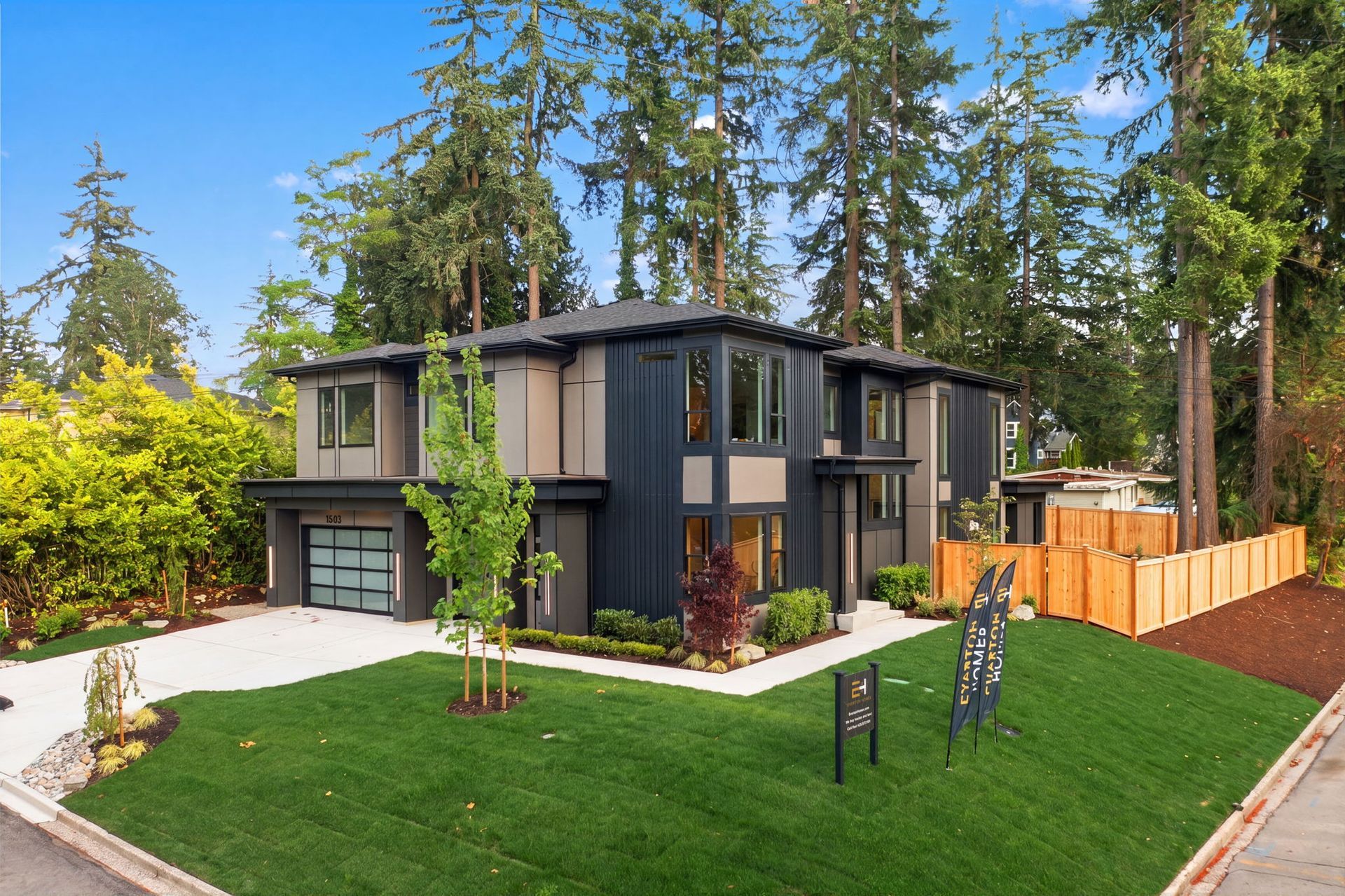 Modern two-story house with dark exterior, white trim, and large green lawn surrounded by tall trees