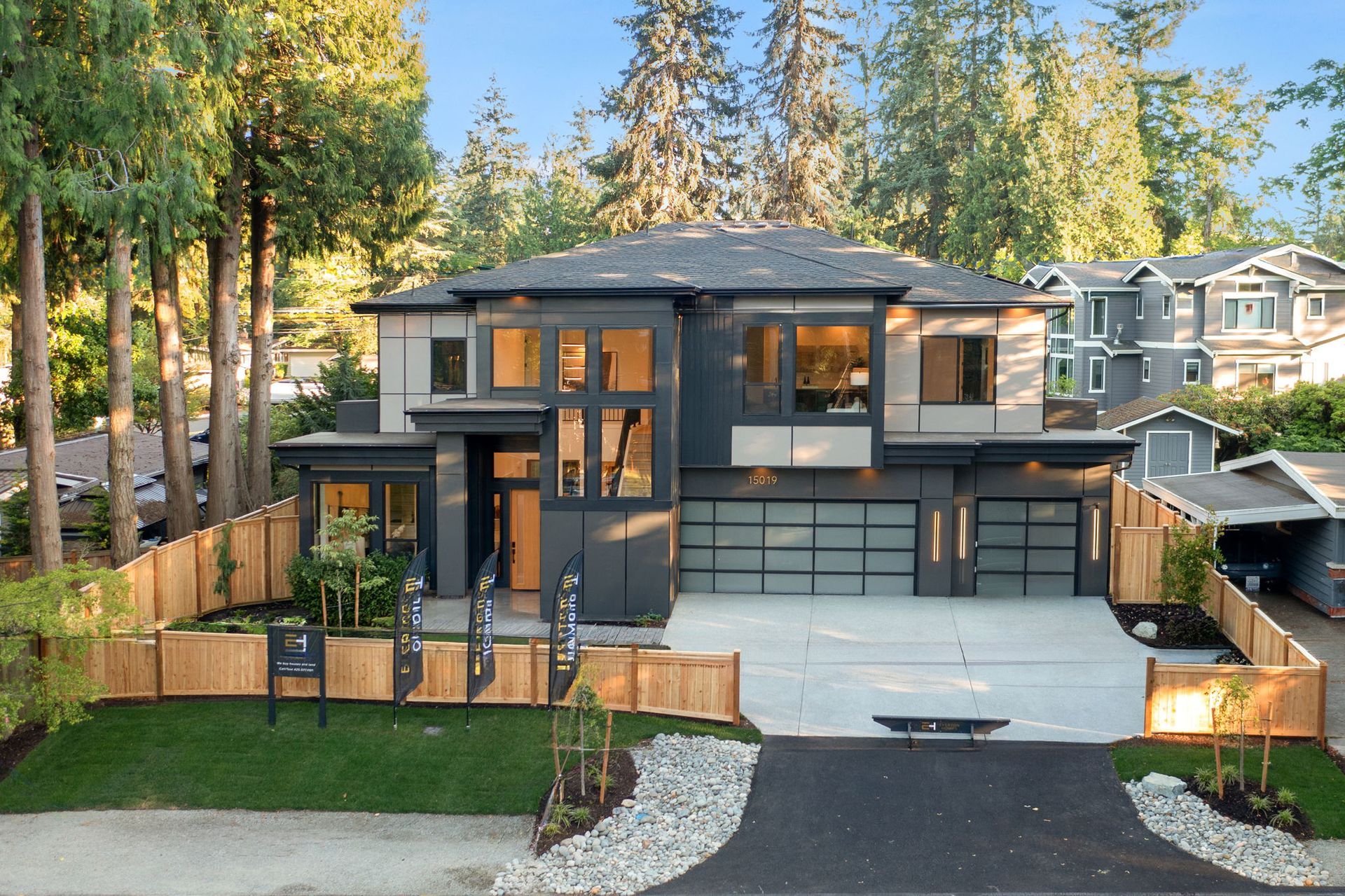 Modern two-story gray house with a front driveway, lawn, and tall trees at sunset