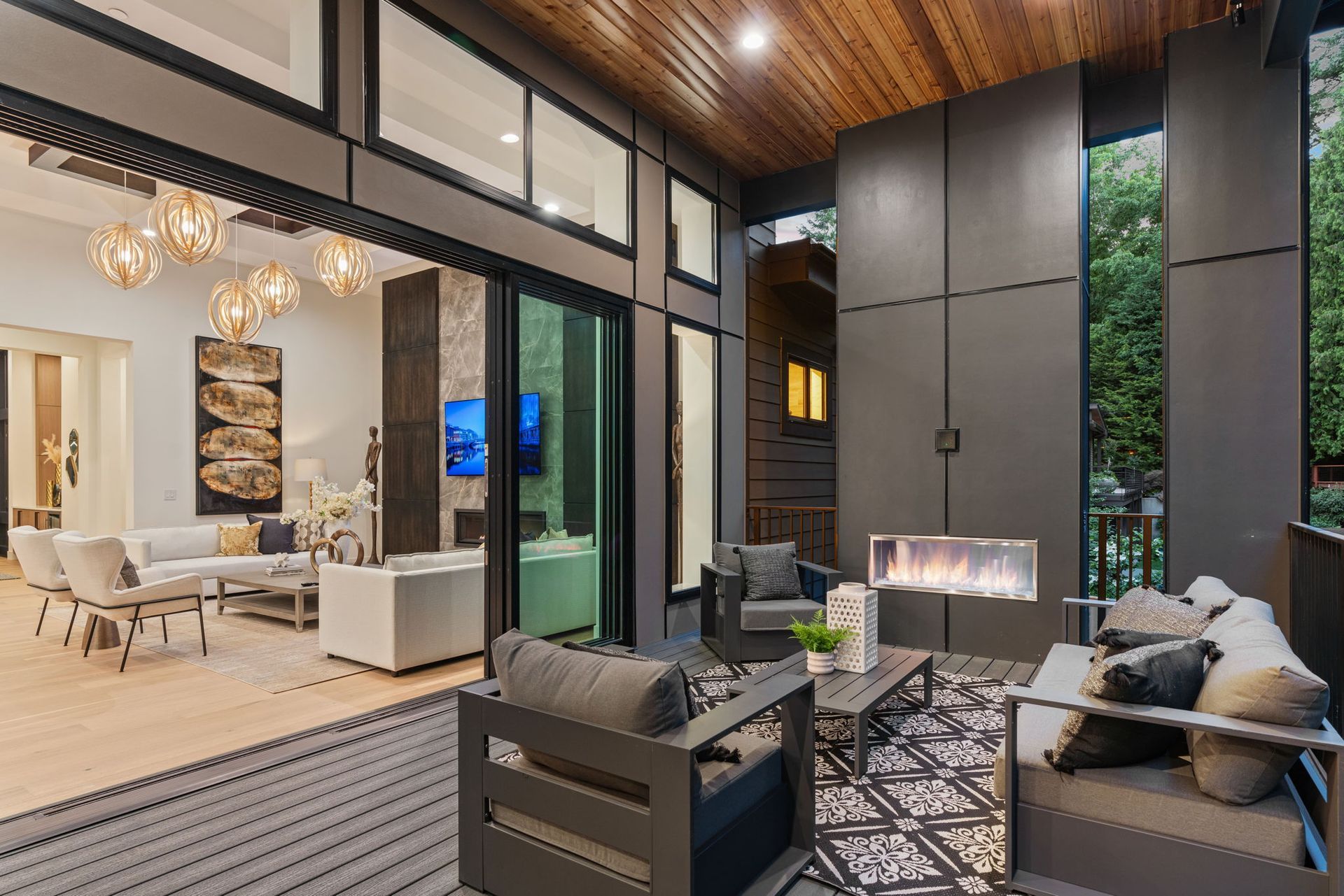 Open-air patio with modern furniture, fireplace, and sliding glass doors leading into a living room.