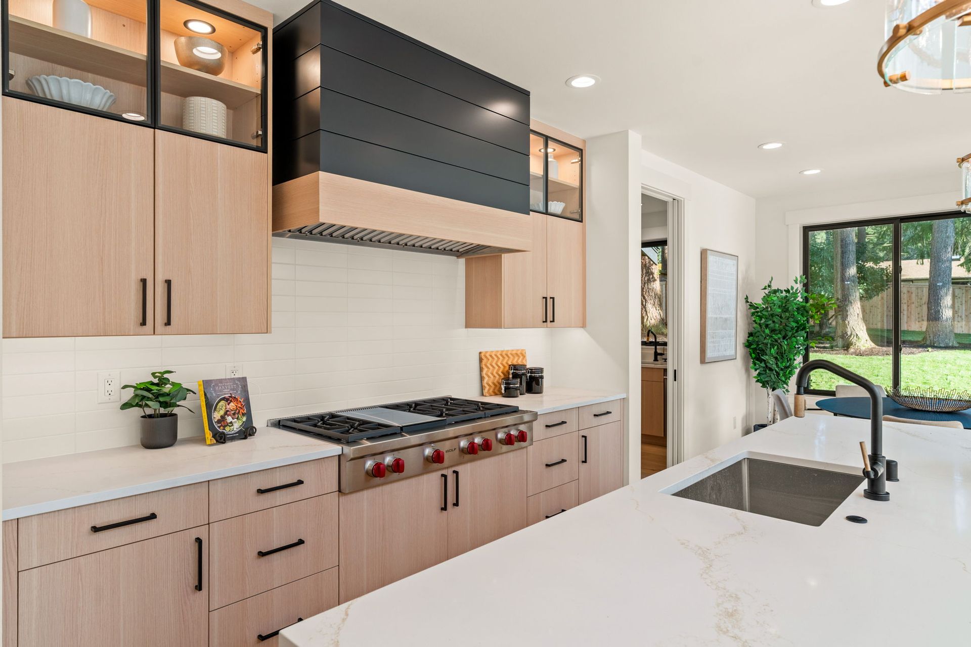 Modern kitchen with light wood cabinets, white countertops, and black range hood.