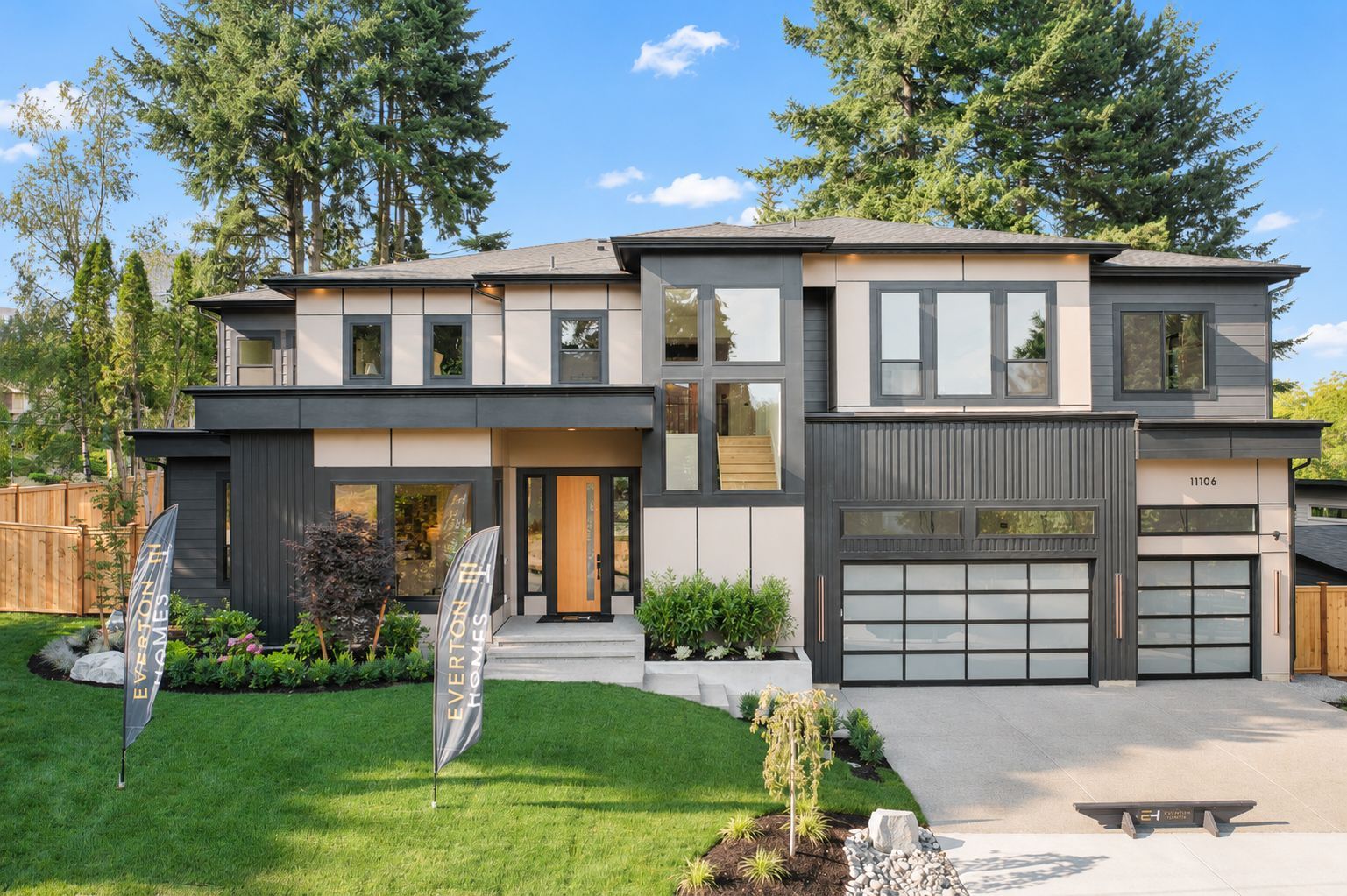 Modern two-story gray house with a front lawn, double garage, and tall trees in the background