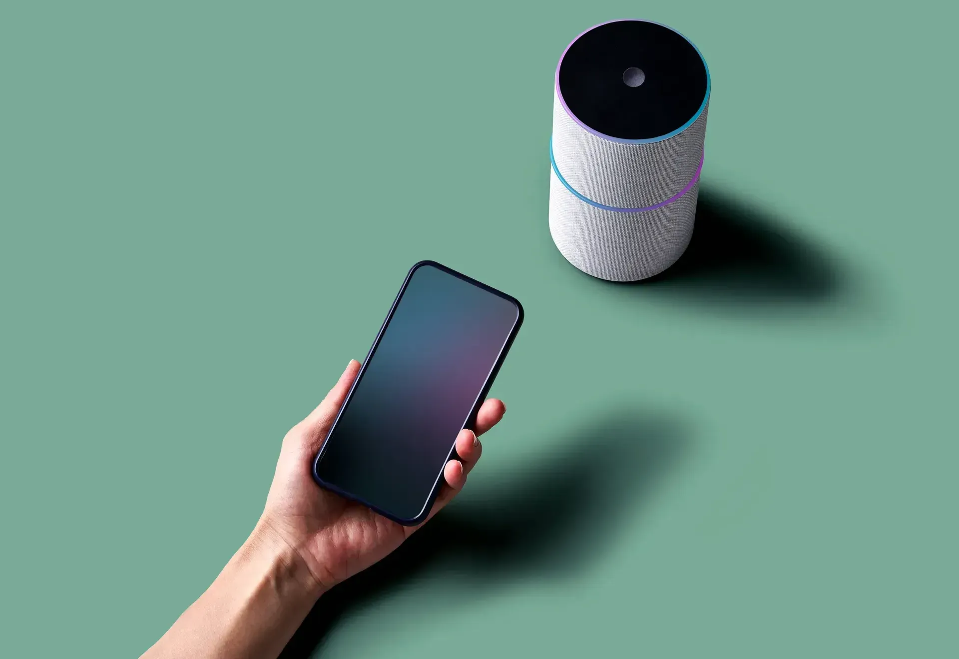 A person is holding a cell phone next to a smart speaker.