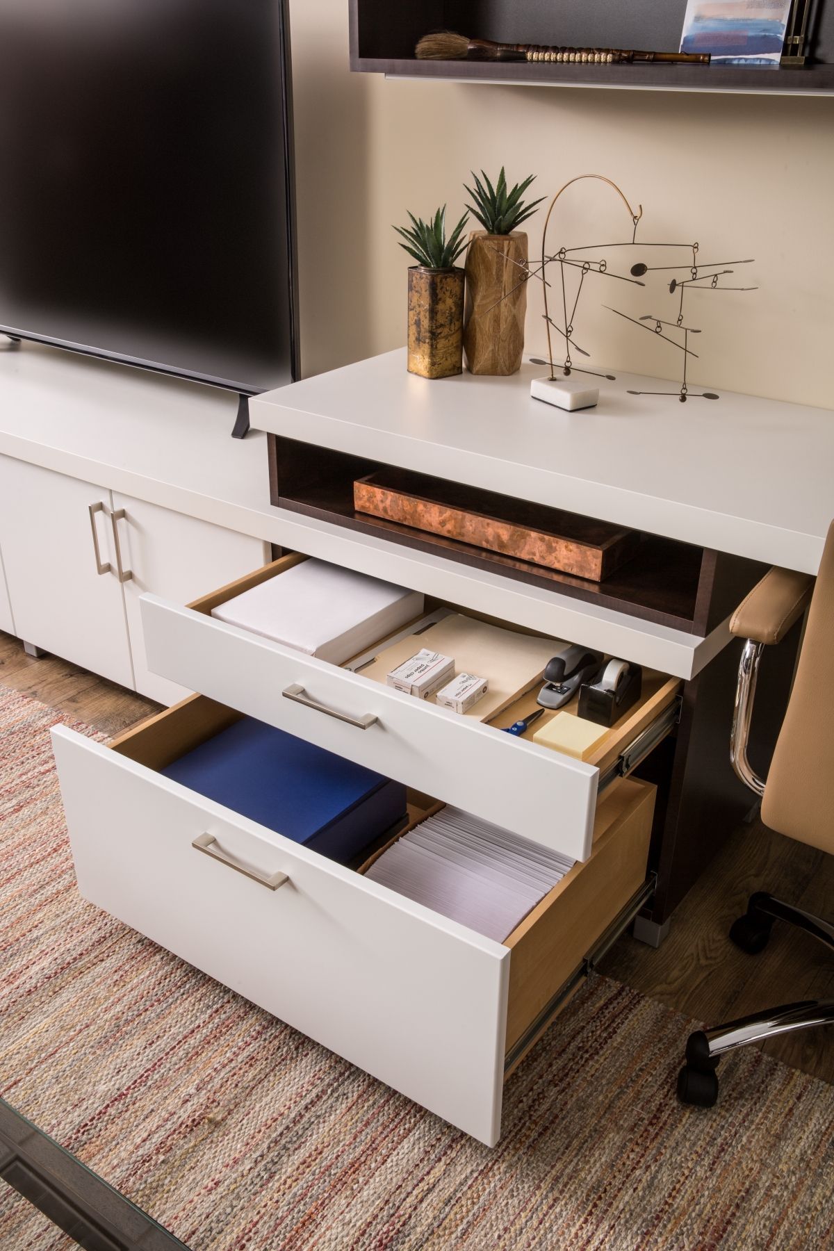 A desk with two drawers open and a tv on the wall.