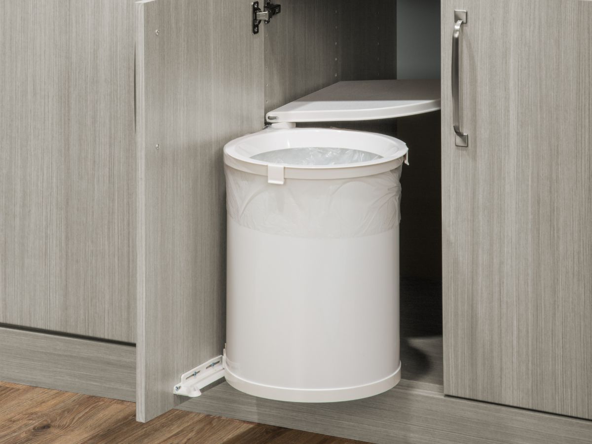 A white trash can is sitting inside of a wooden cabinet.