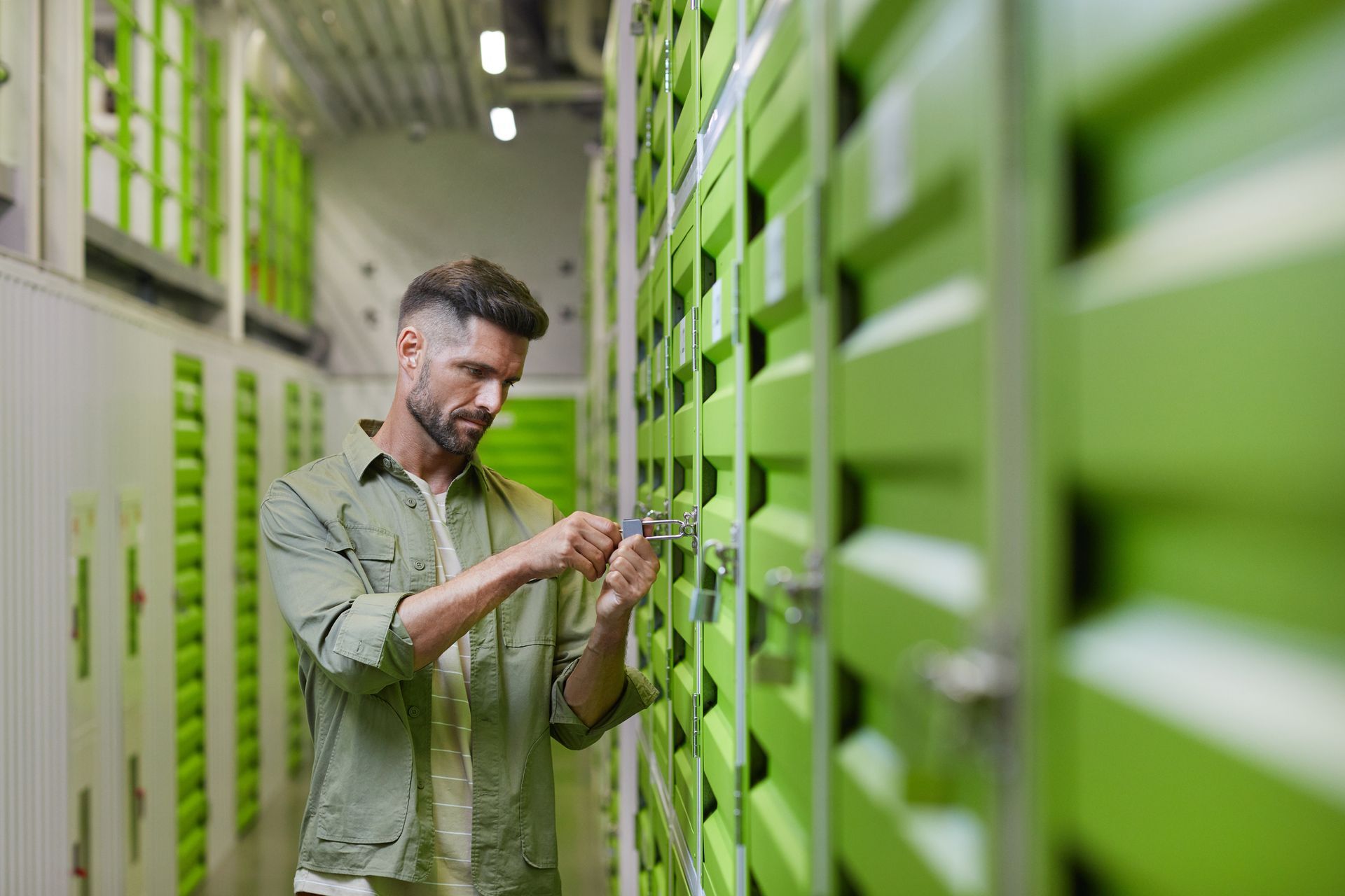Man unlocking mini storage unit door at secure self-storage facility.