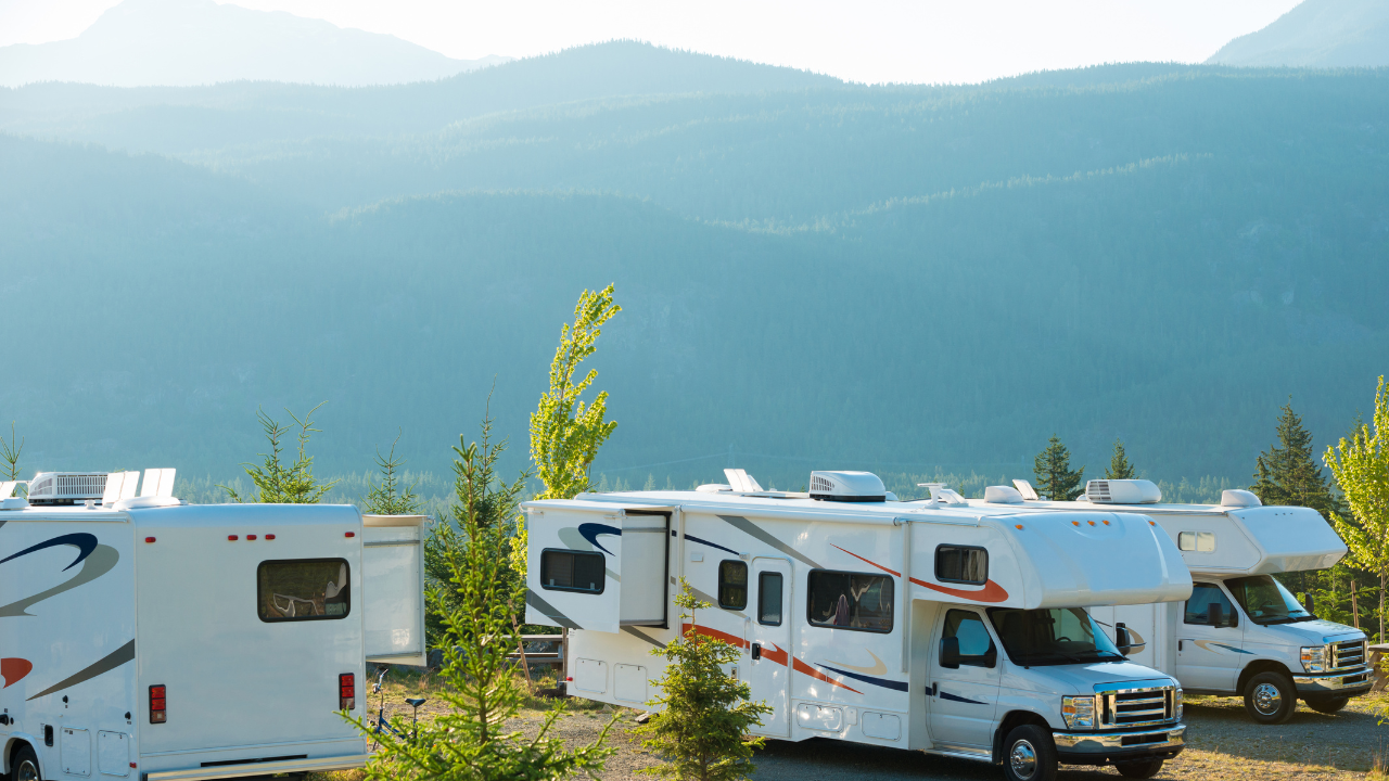 RVs parked at a campground with mountains in the background under a blue sky.