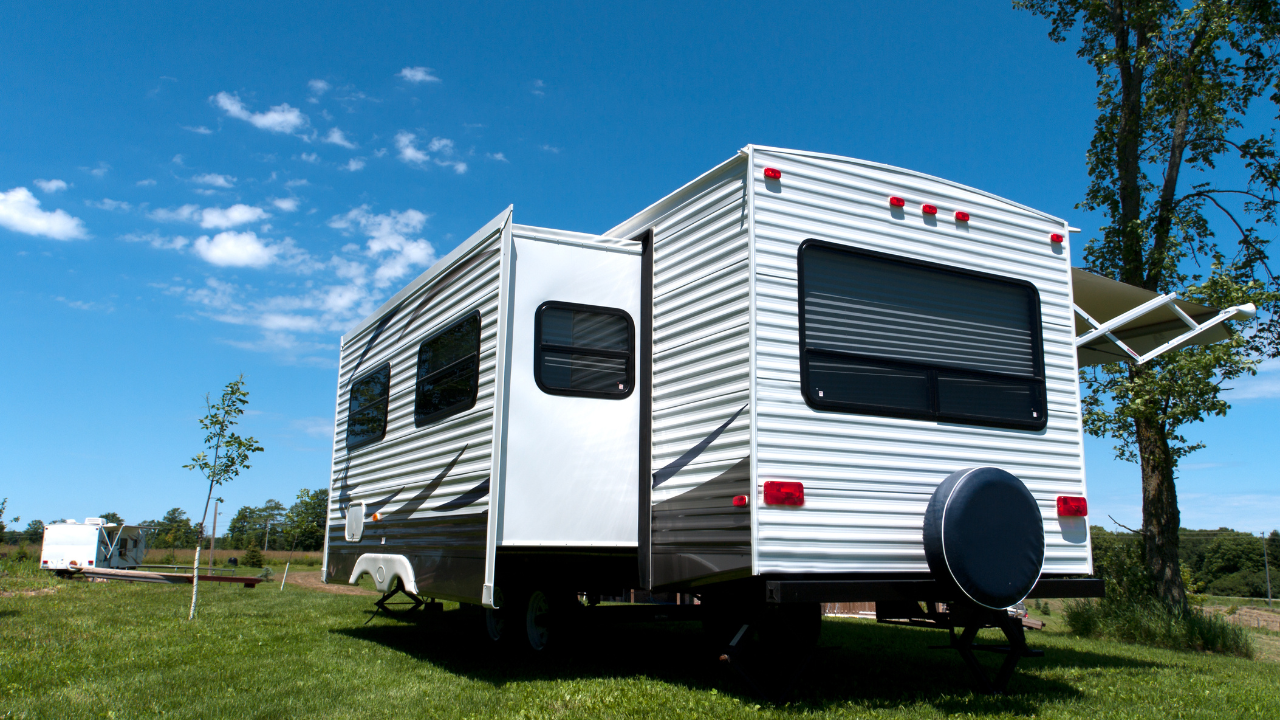 White RV parked on grass, door open, with blue sky and trees in the background.