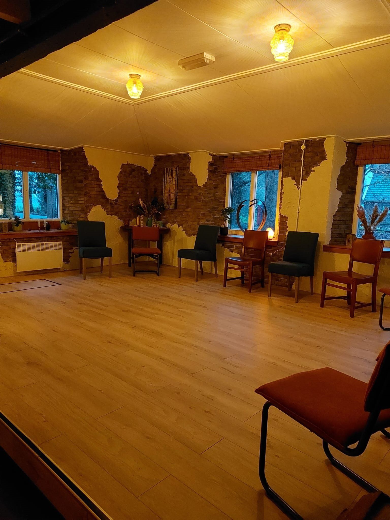Een lege dansstudio met houten vloer, stoelen langs de muren en warme plafondverlichting.