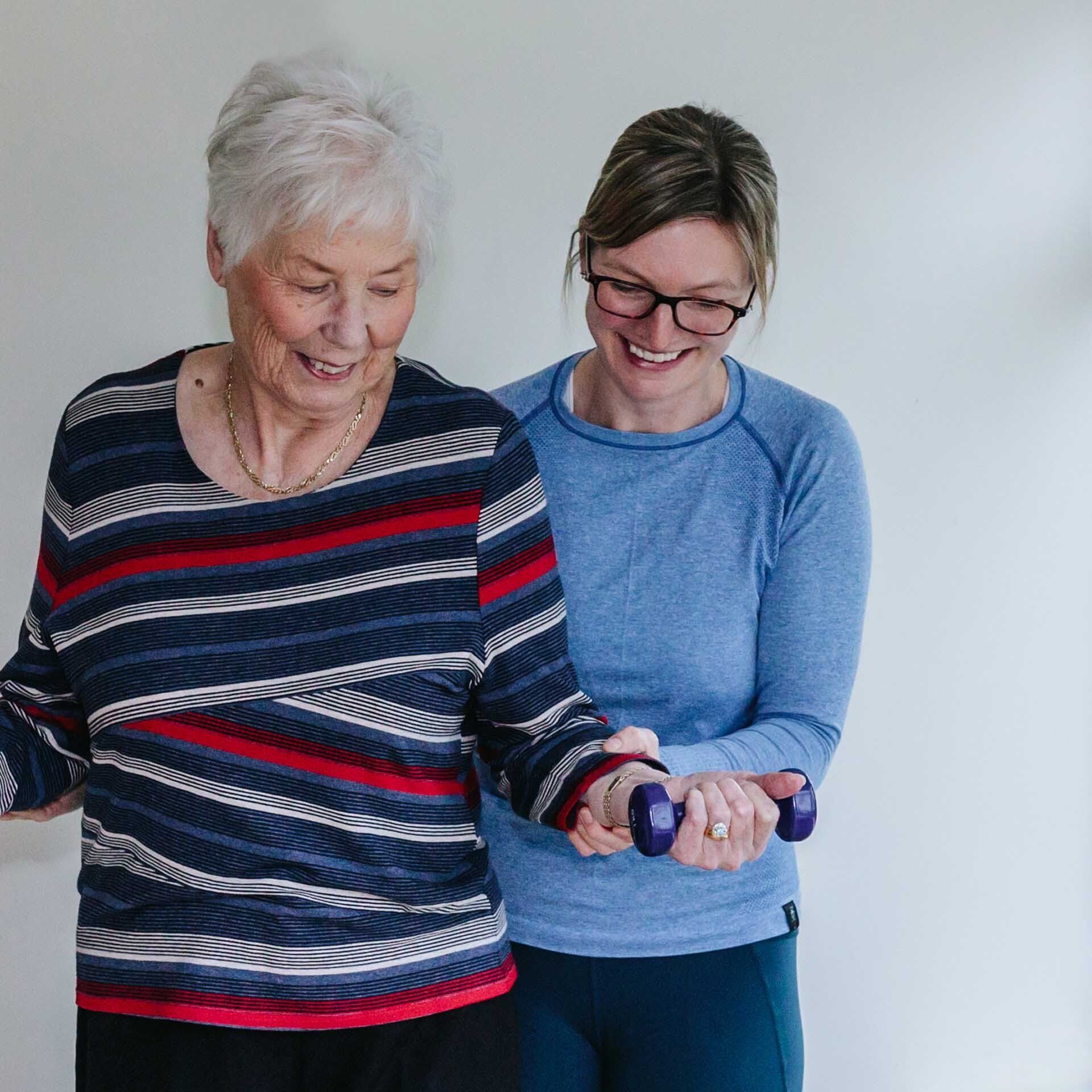 Two women are standing next to each other holding dumbbells.
