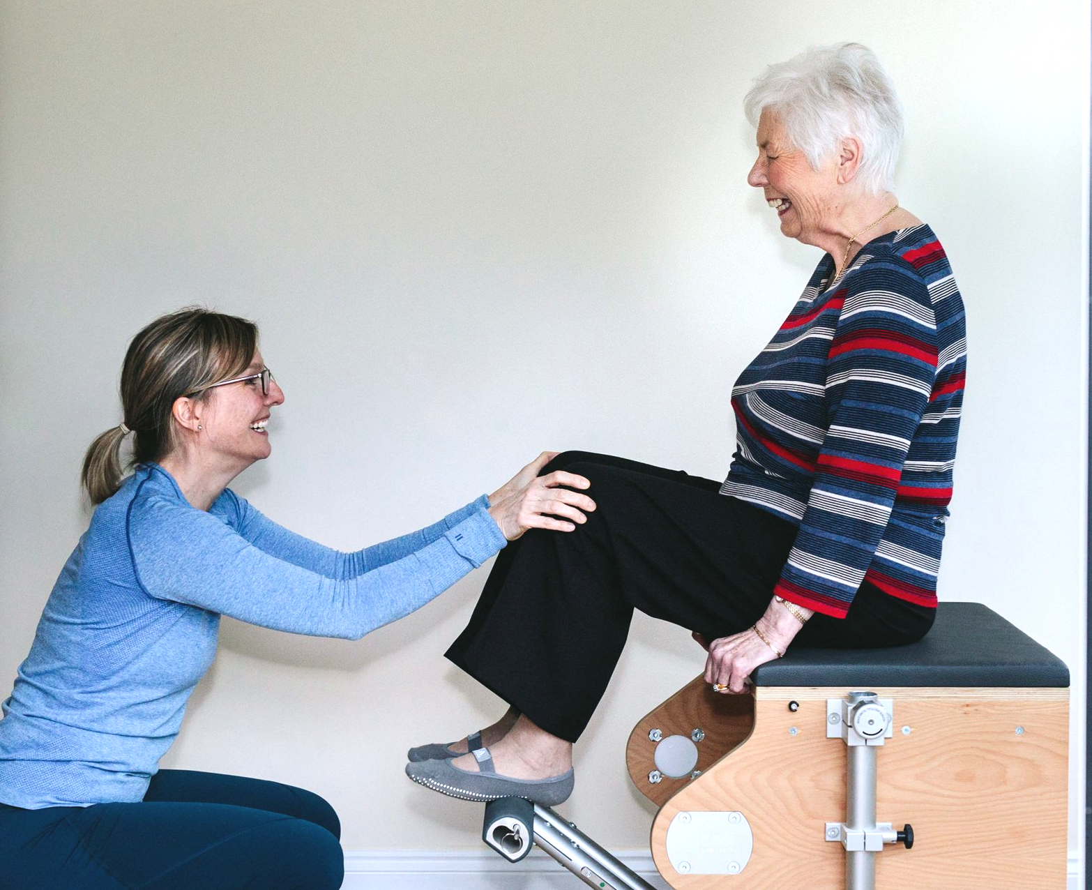 A woman is helping an older woman sit on a pilates machine.