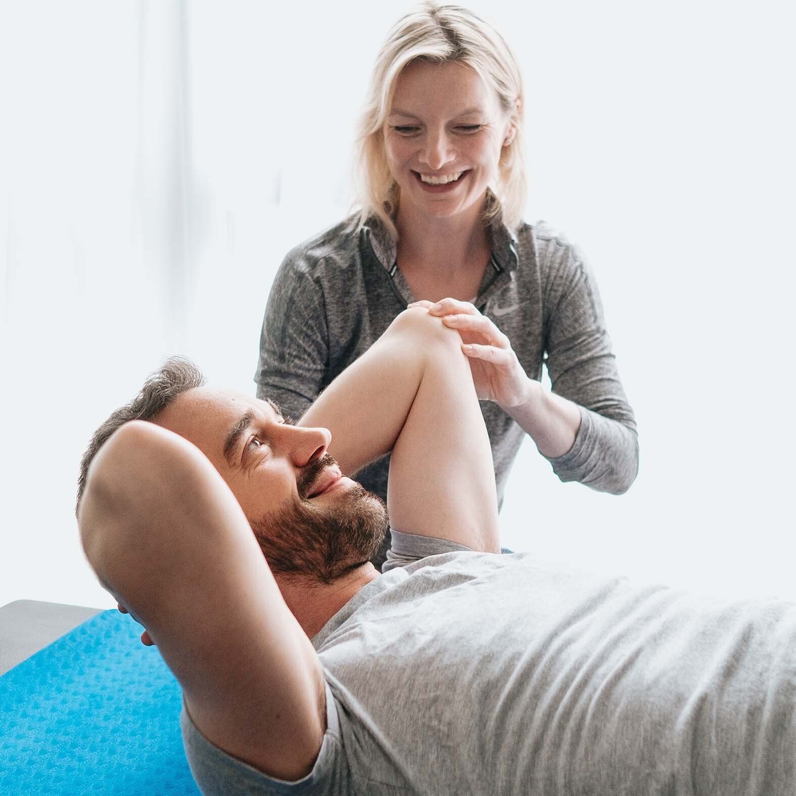 A woman is helping a man stretch his arms on a yoga mat.