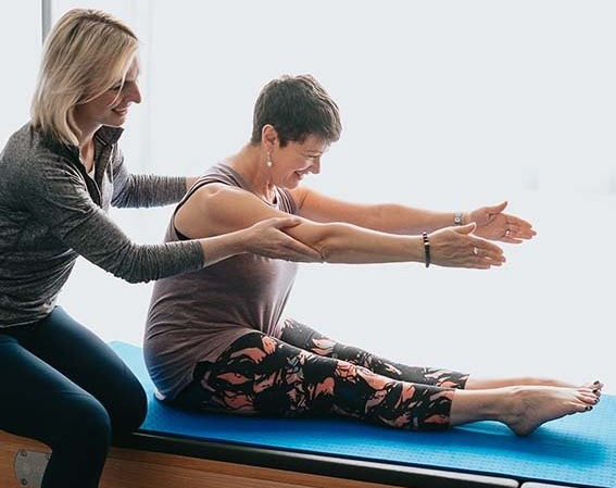 A woman is helping another woman do exercises on a mat.
