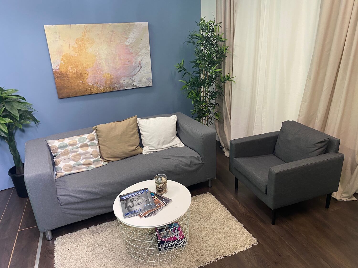 Ein Wohnzimmer mit Sofa, Sessel, Tisch und einem Gemälde an der Wand.