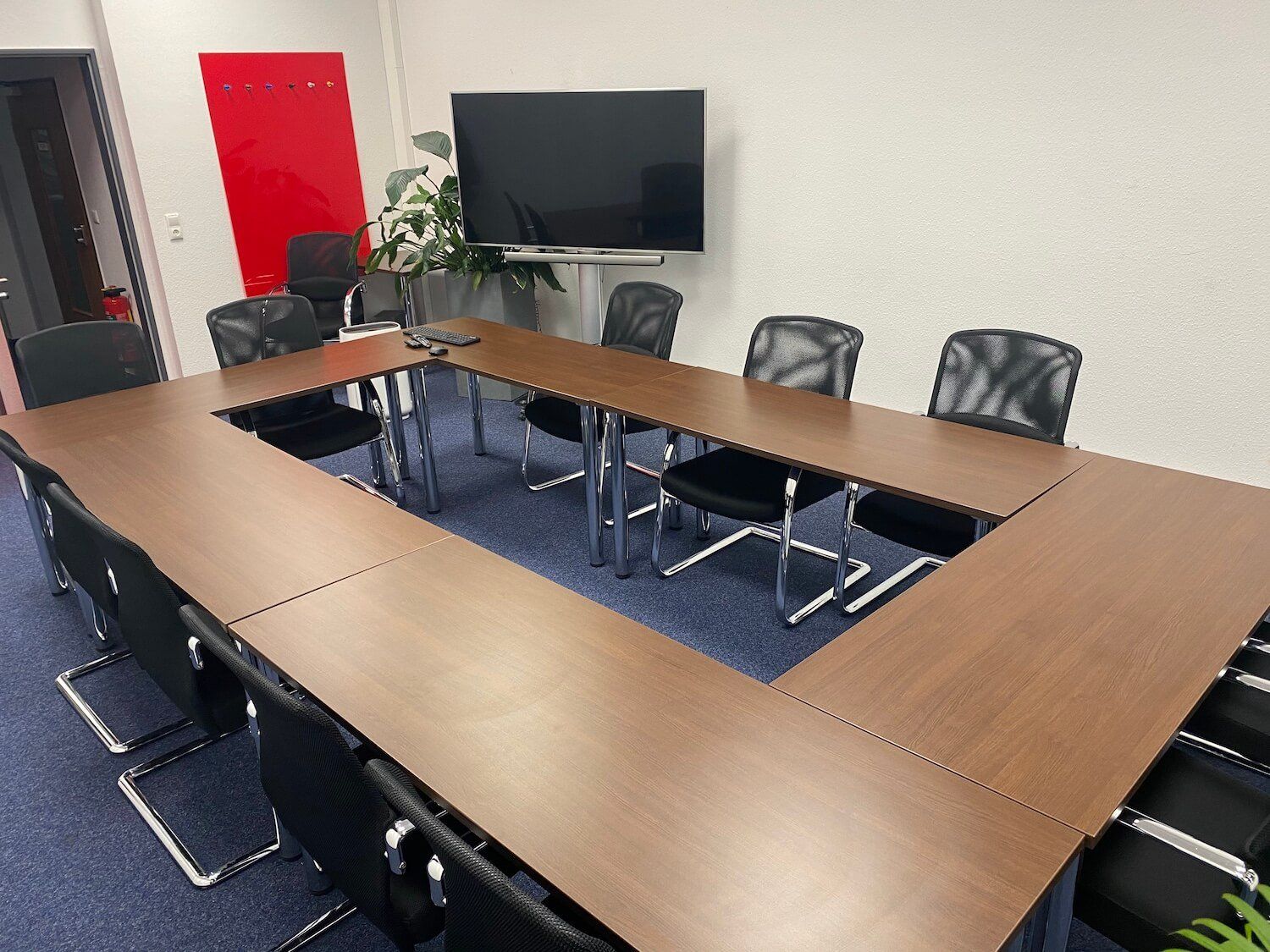Ein Konferenzraum mit einem langen Tisch und Stühlen sowie einem Flachbildfernseher.