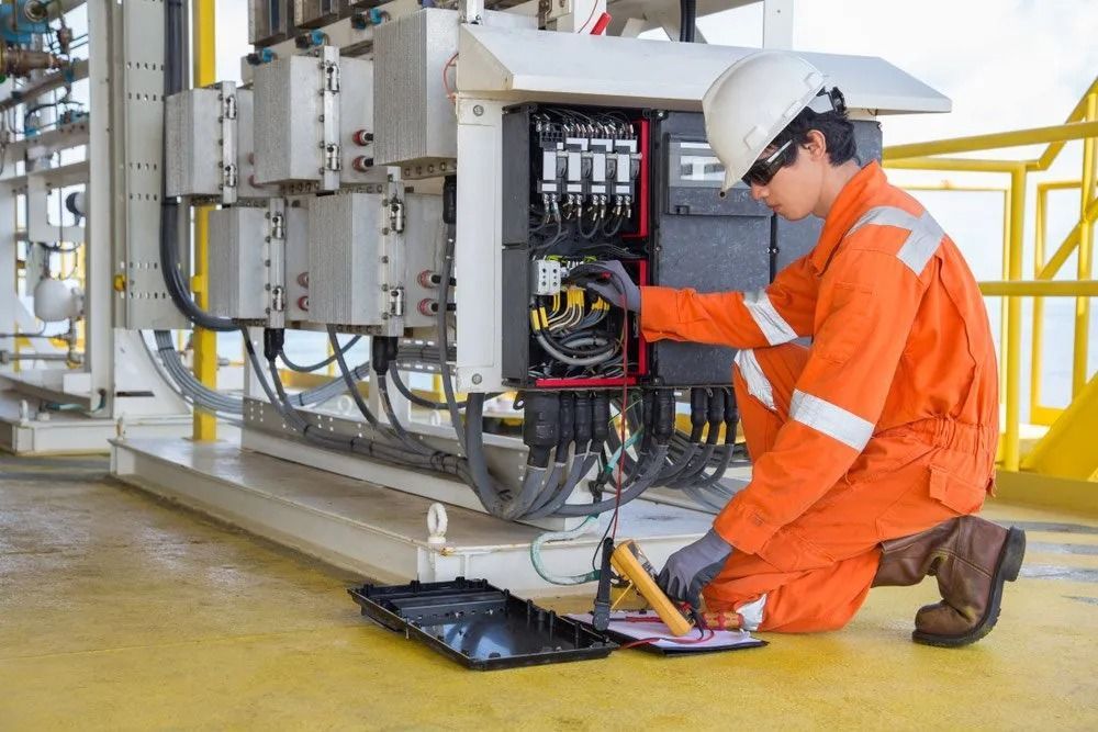 Technician in orange coveralls kneeling, inspecting electrical equipment on an offshore platform. — Fire Maintenance Services (NT) Pty Ltd in Winnellie, NT