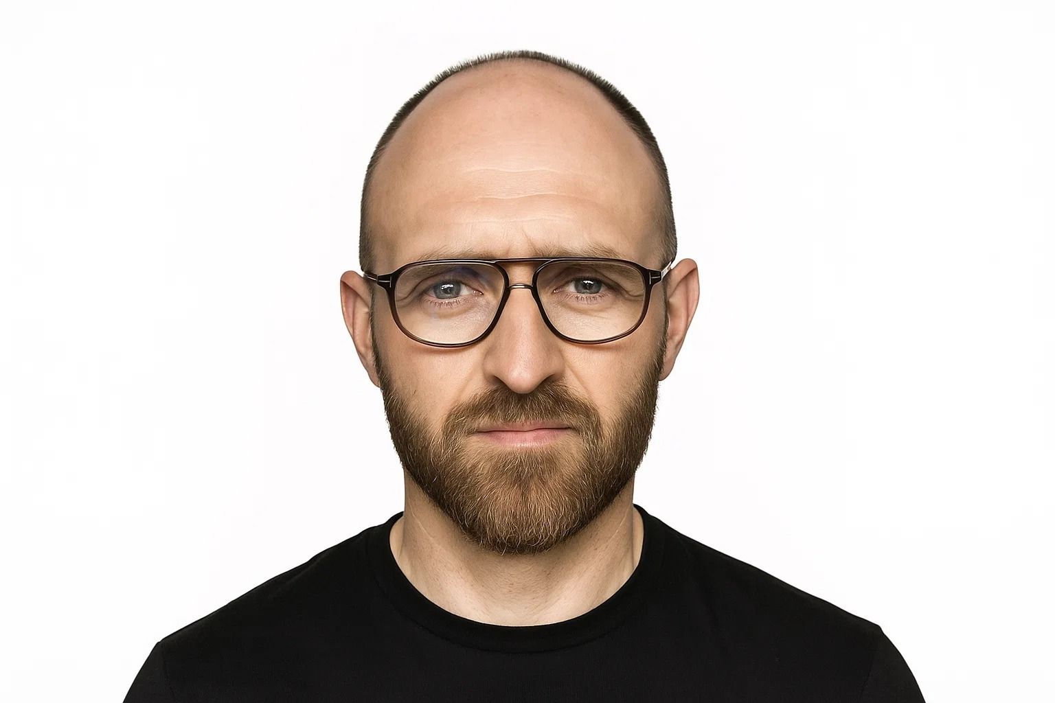 Un hombre con barba corta y gafas, mirando directamente a la cámara sobre un fondo blanco.