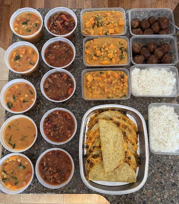 Tray of assorted Indian dishes in clear containers, including curries, rice, and bread arranged in a meal spread.