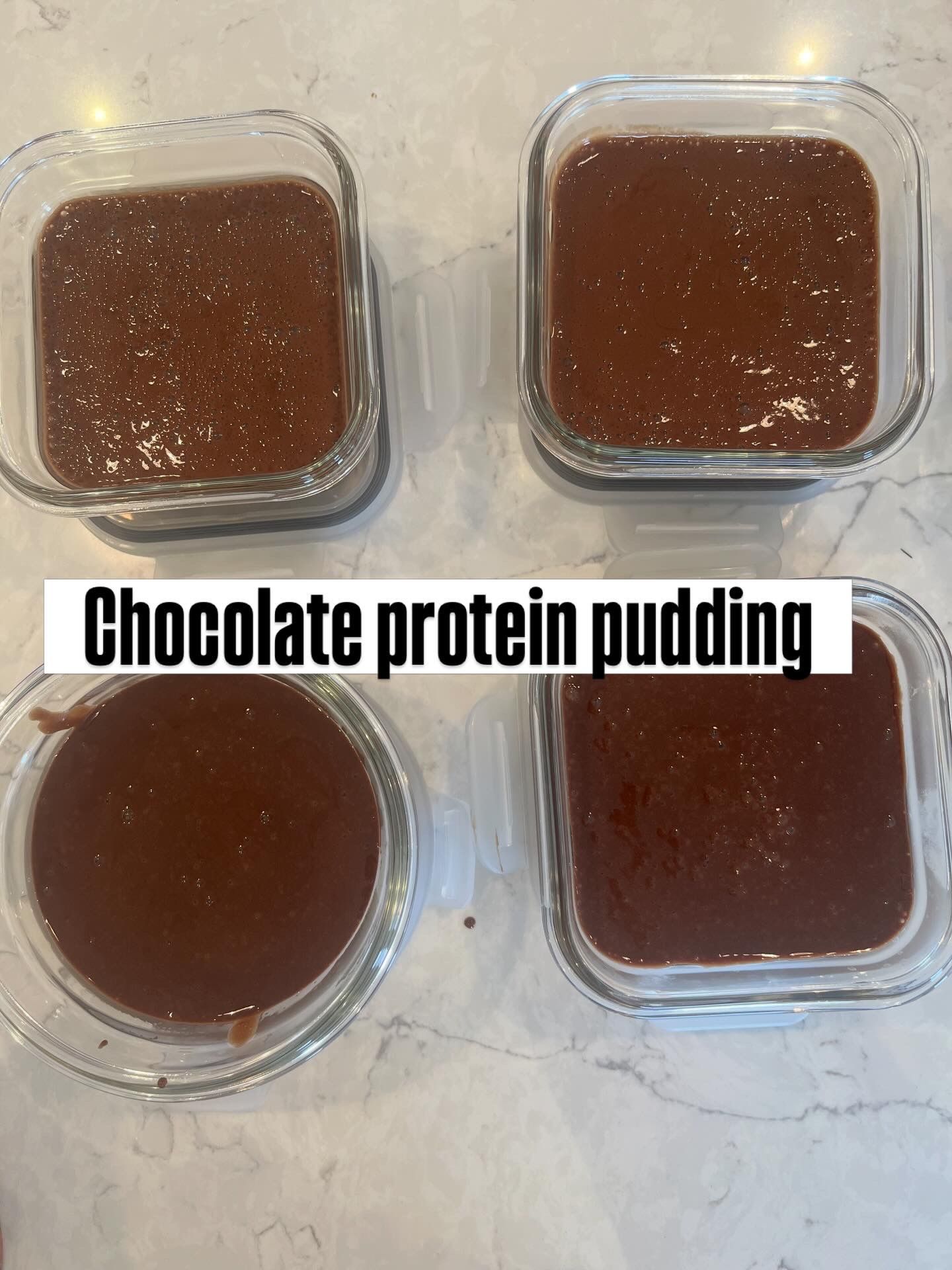 Four containers of chocolate protein pudding on a light countertop, labeled in the center.