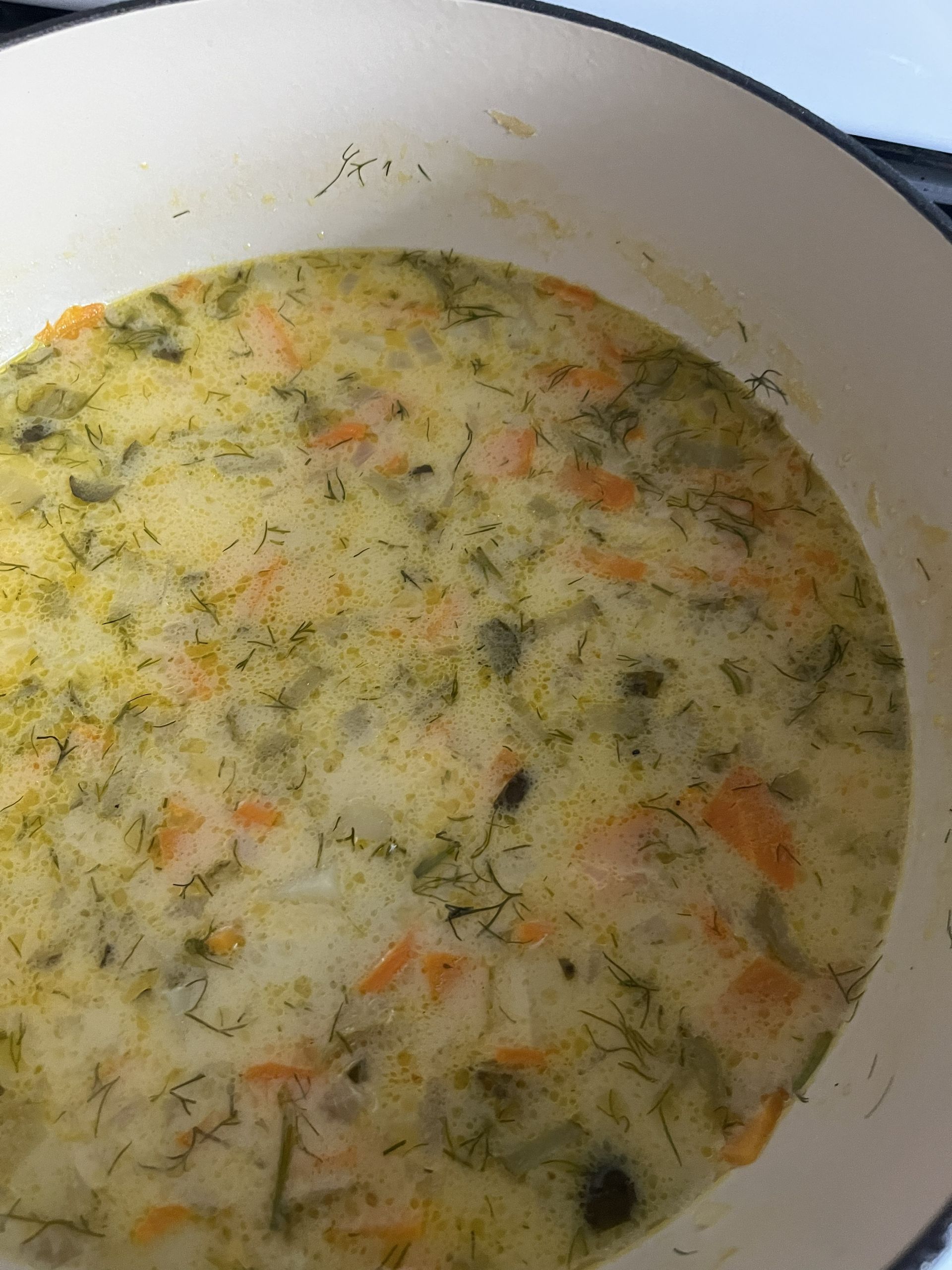 A pot of creamy vegetable soup with herbs and diced vegetables simmering inside.