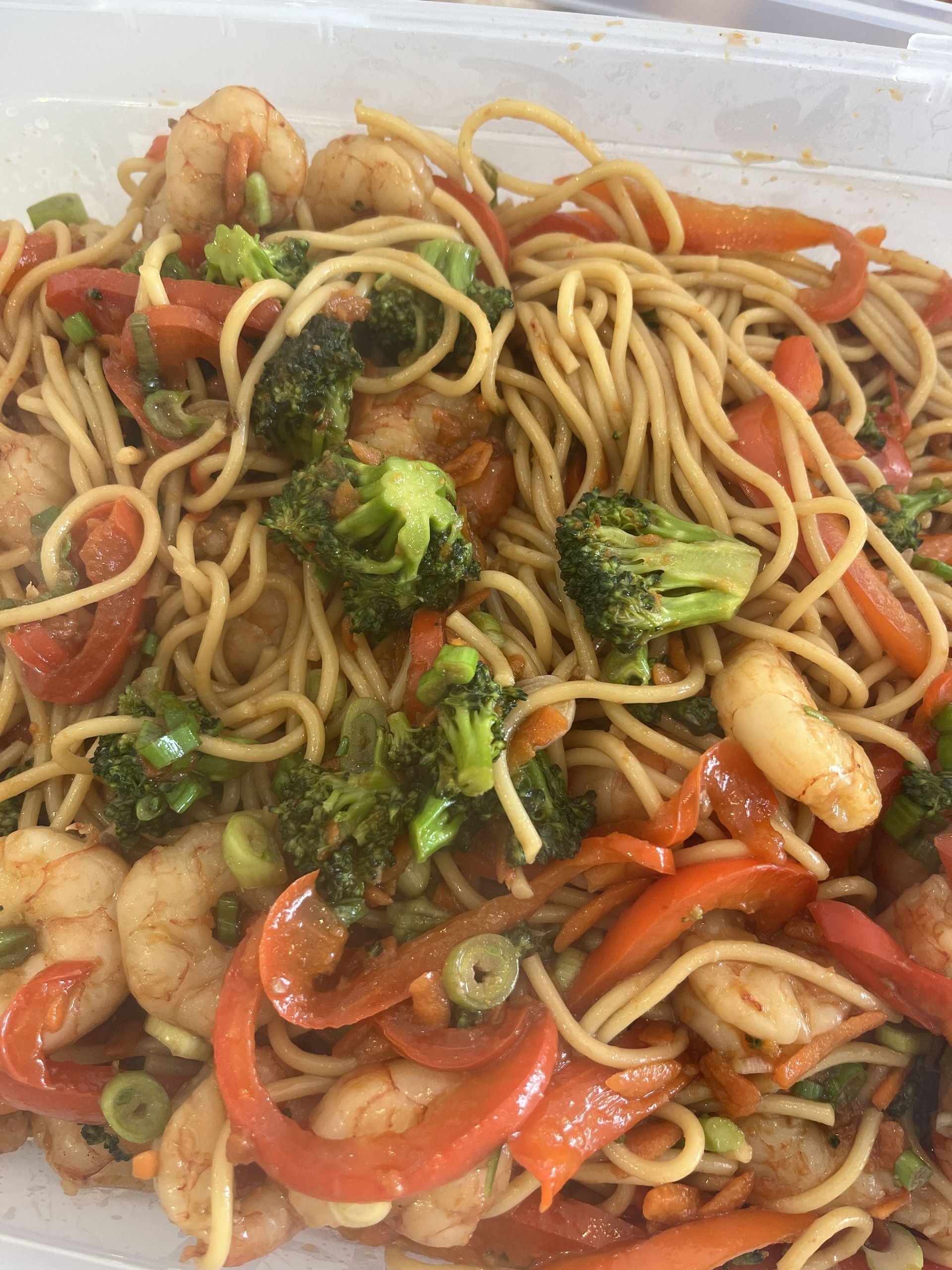 Stir-fried noodles with broccoli, shrimp, and red peppers in a takeout container
