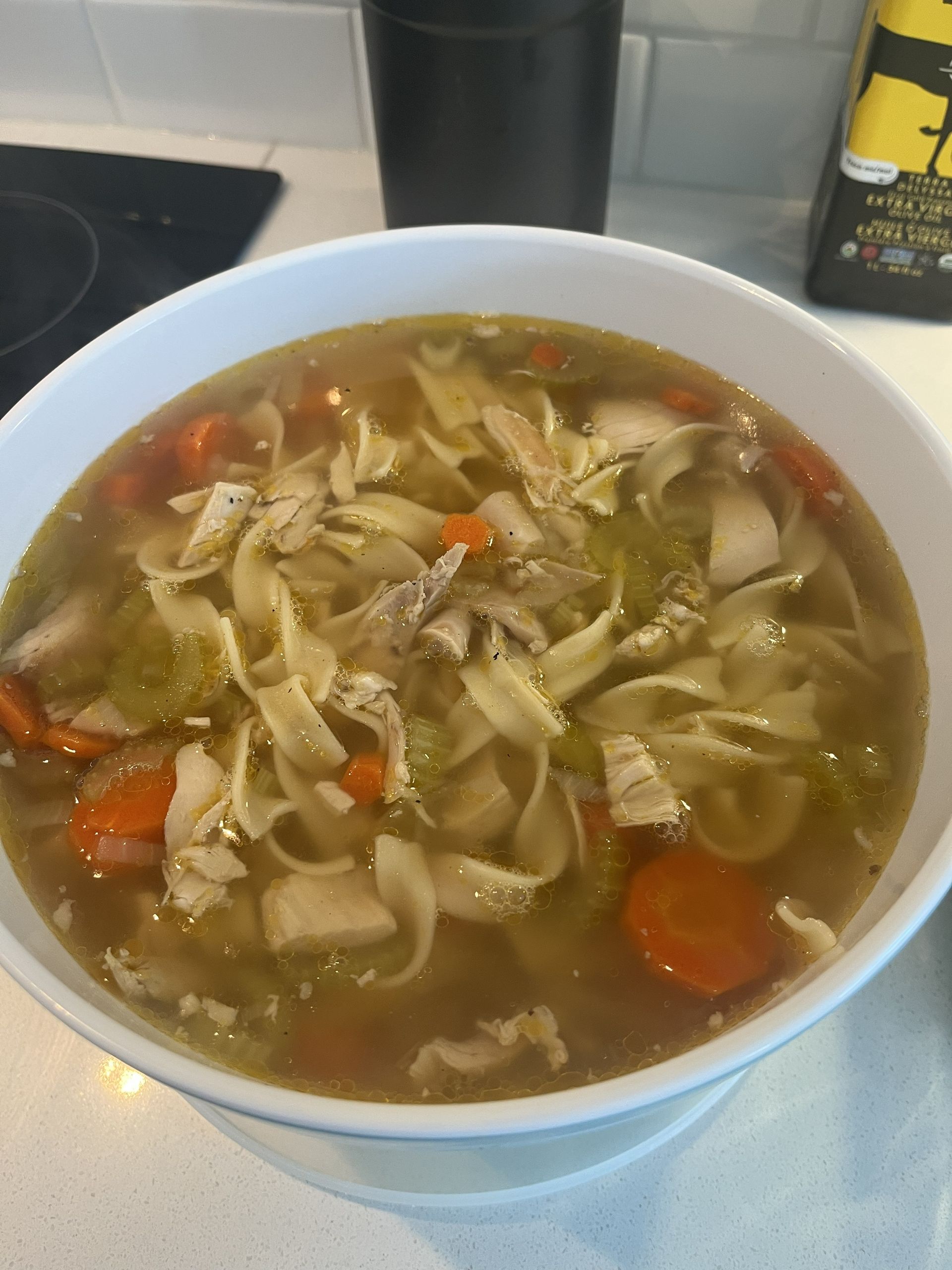A bowl of chicken noodle soup with carrots and cabbage on a kitchen counter.
