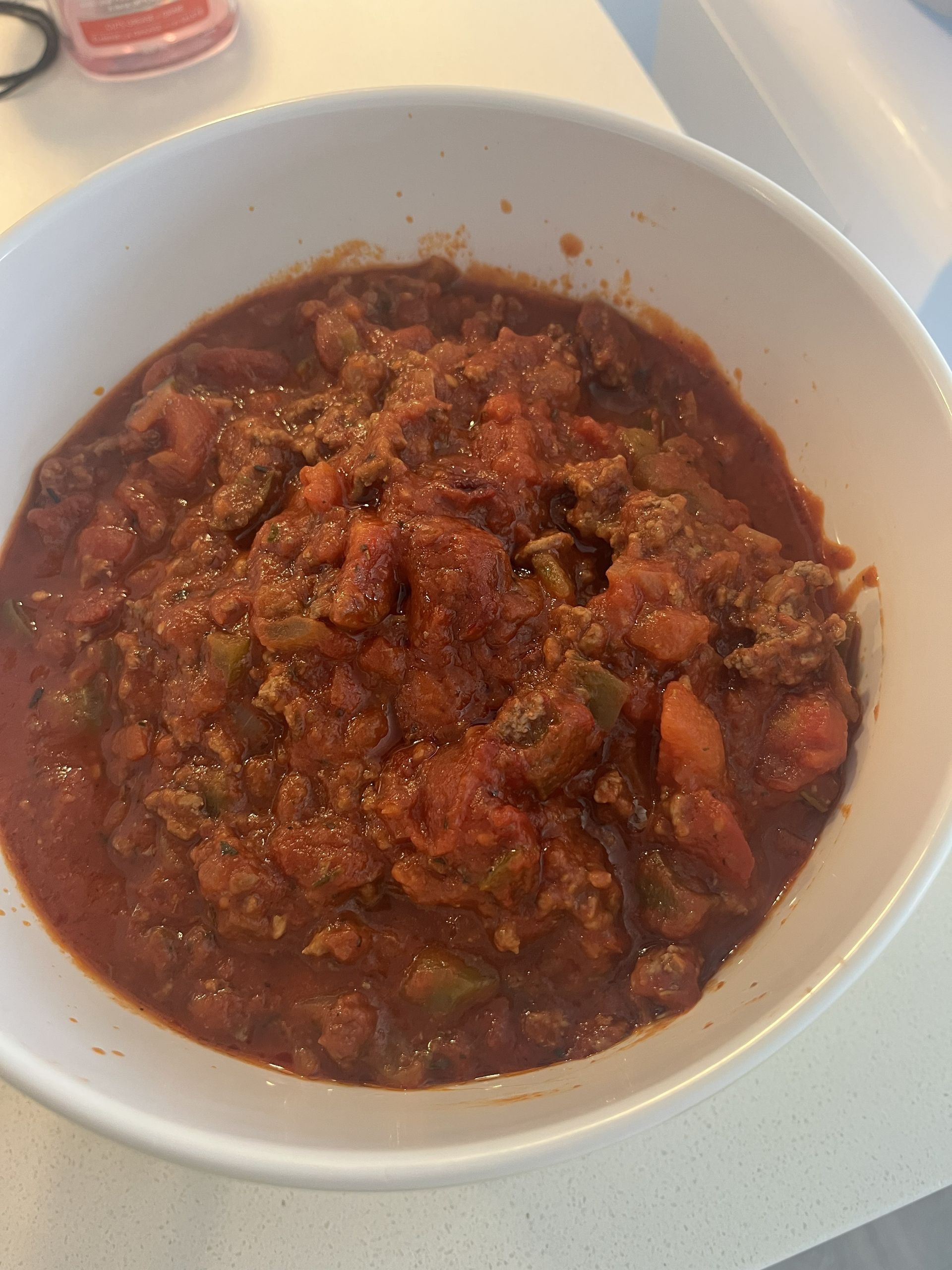 White bowl of chunky red-brown stew or chili on a light tabletop.