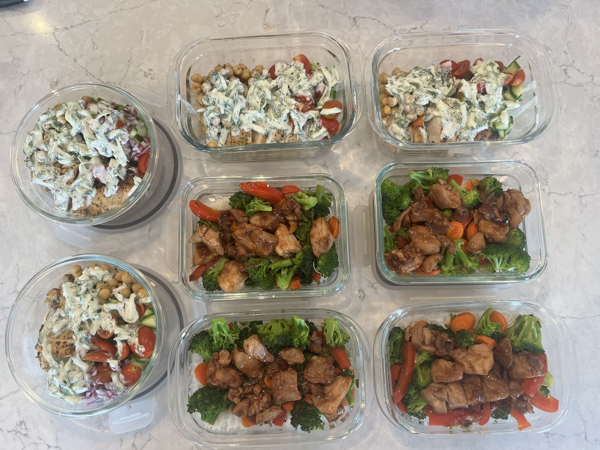 Six meal-prep containers with rice, vegetables, and seasoned meat on a light countertop.