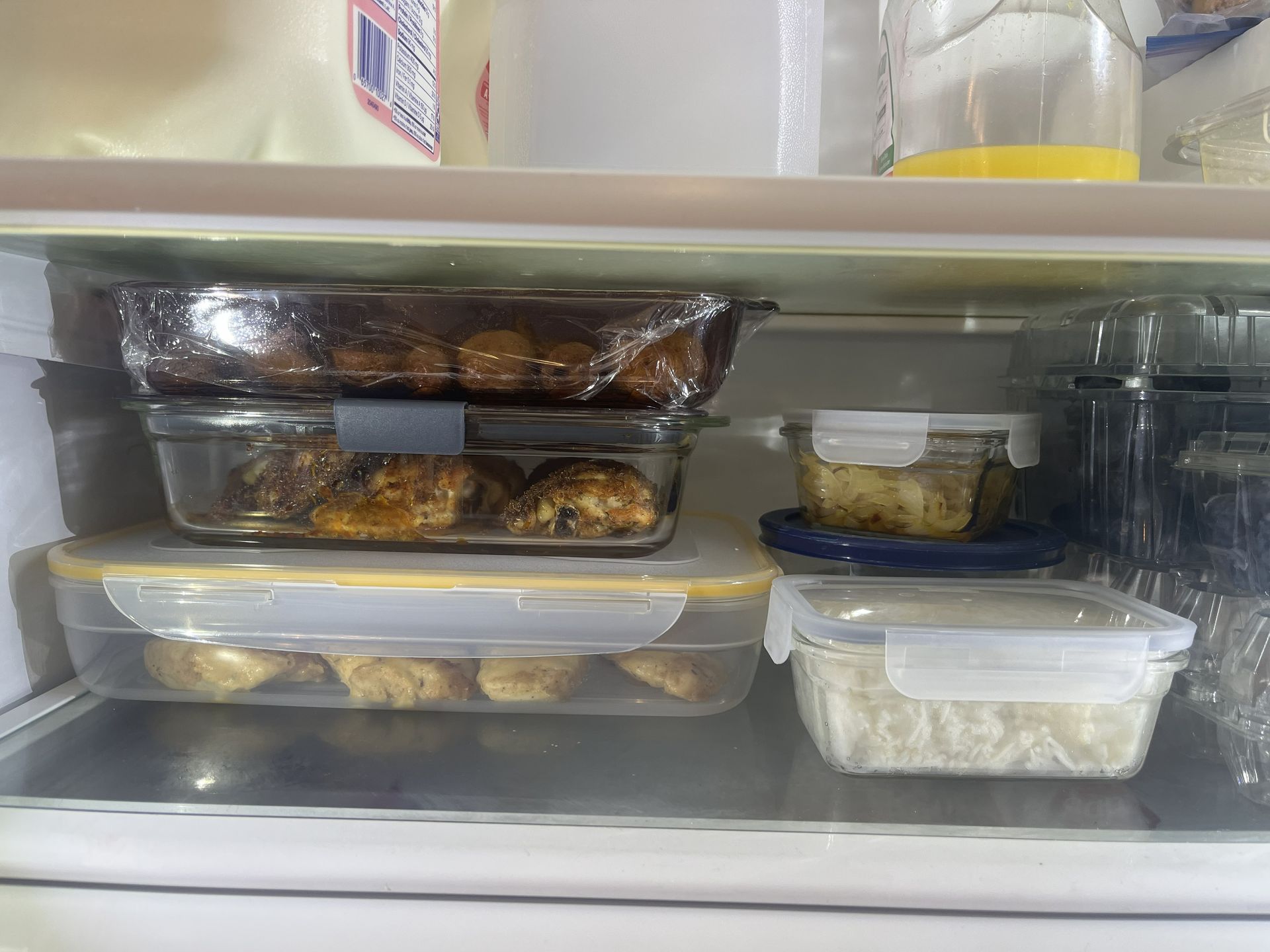 Refrigerator shelf with stacked meal containers and leftovers in clear and black plastic tubs