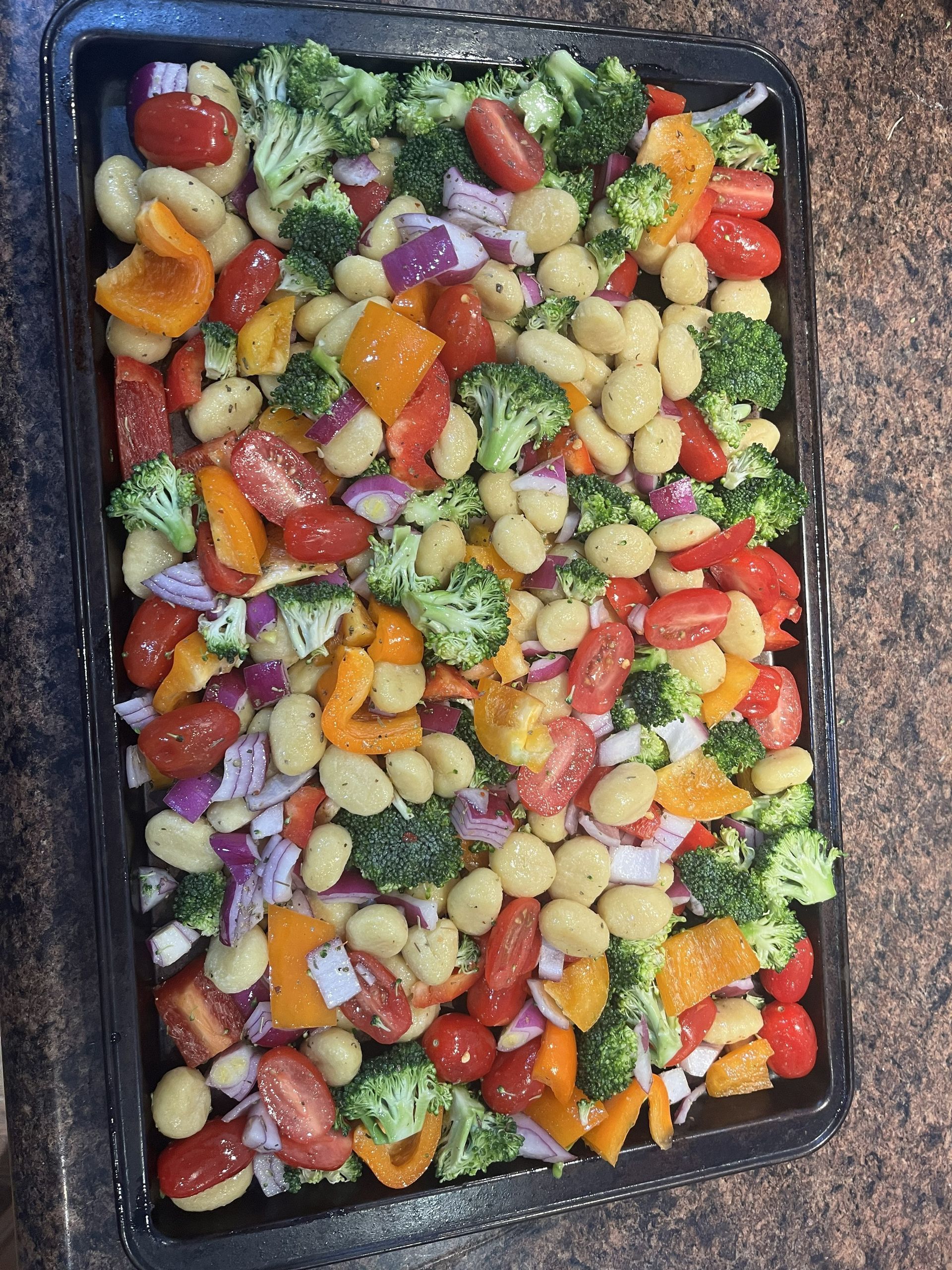 Tray of mixed frozen vegetables and potatoes in a dark baking pan