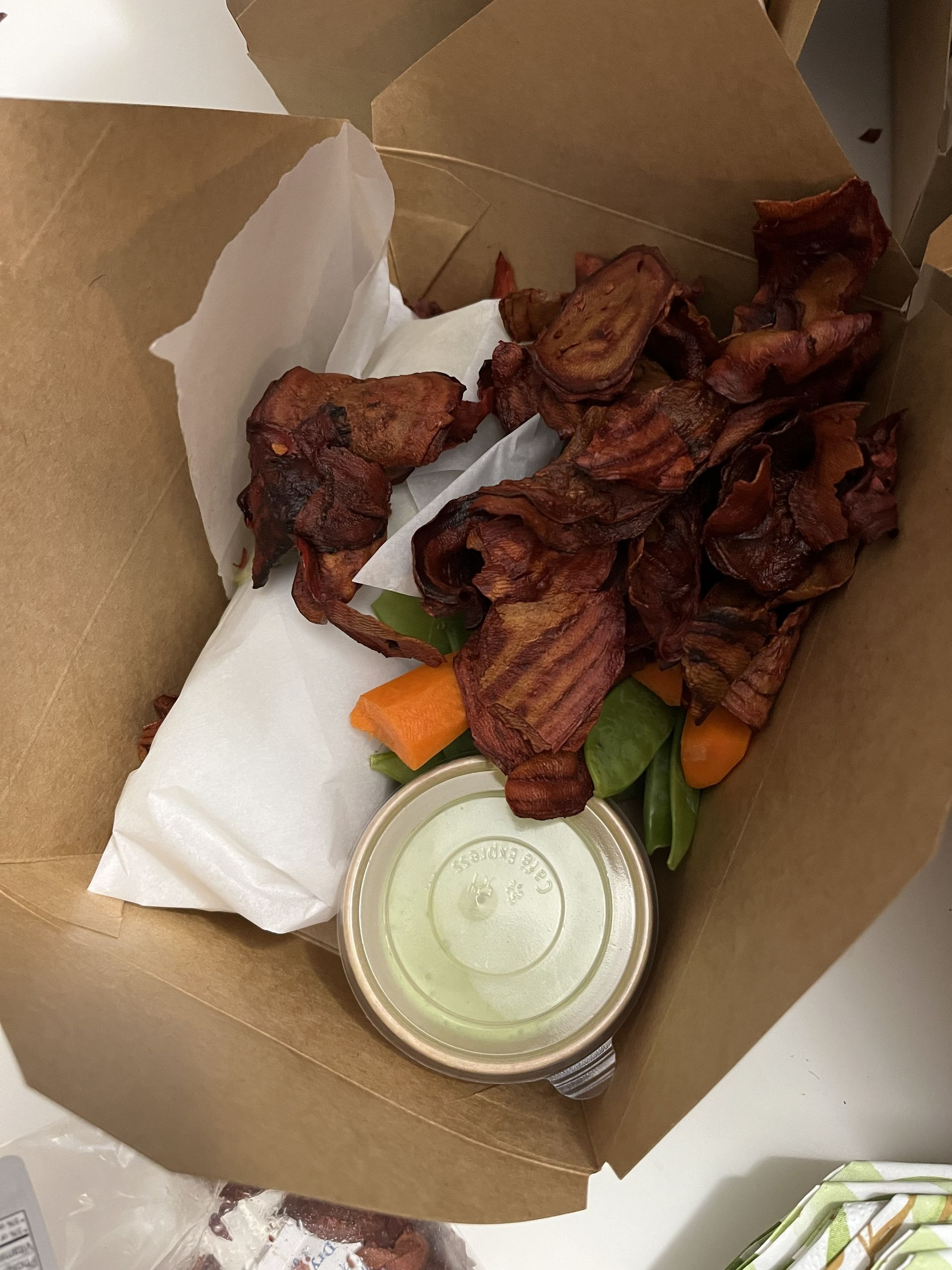 Takeout box with grilled chicken wings, carrot and celery sticks, and a small cup of dipping sauce