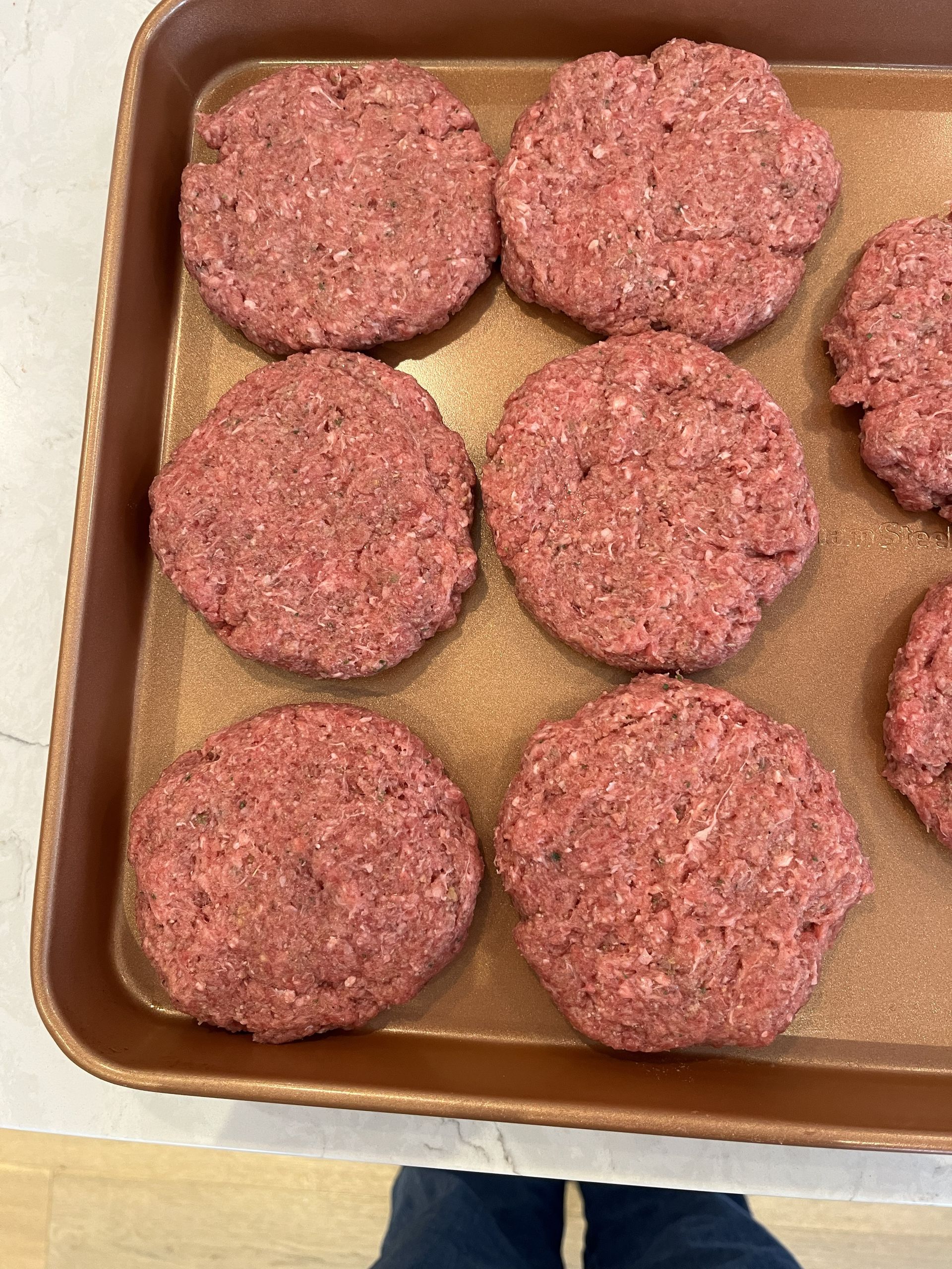 Tray of six raw hamburger patties on parchment paper, with one partially visible on the right.