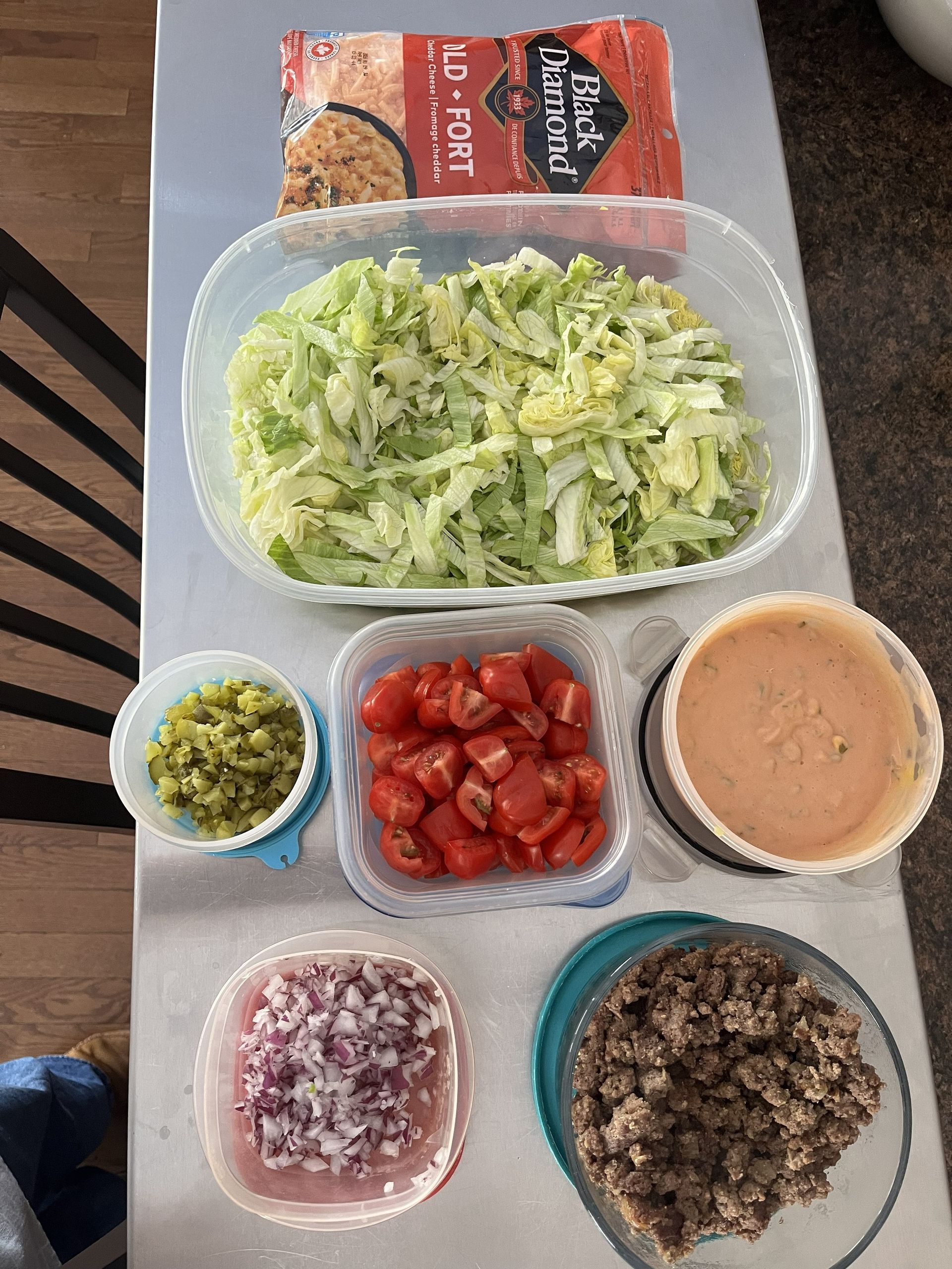 Meal prep containers with shredded lettuce, diced tomatoes, chopped onions, ground meat, salsa, and a packaged food item.