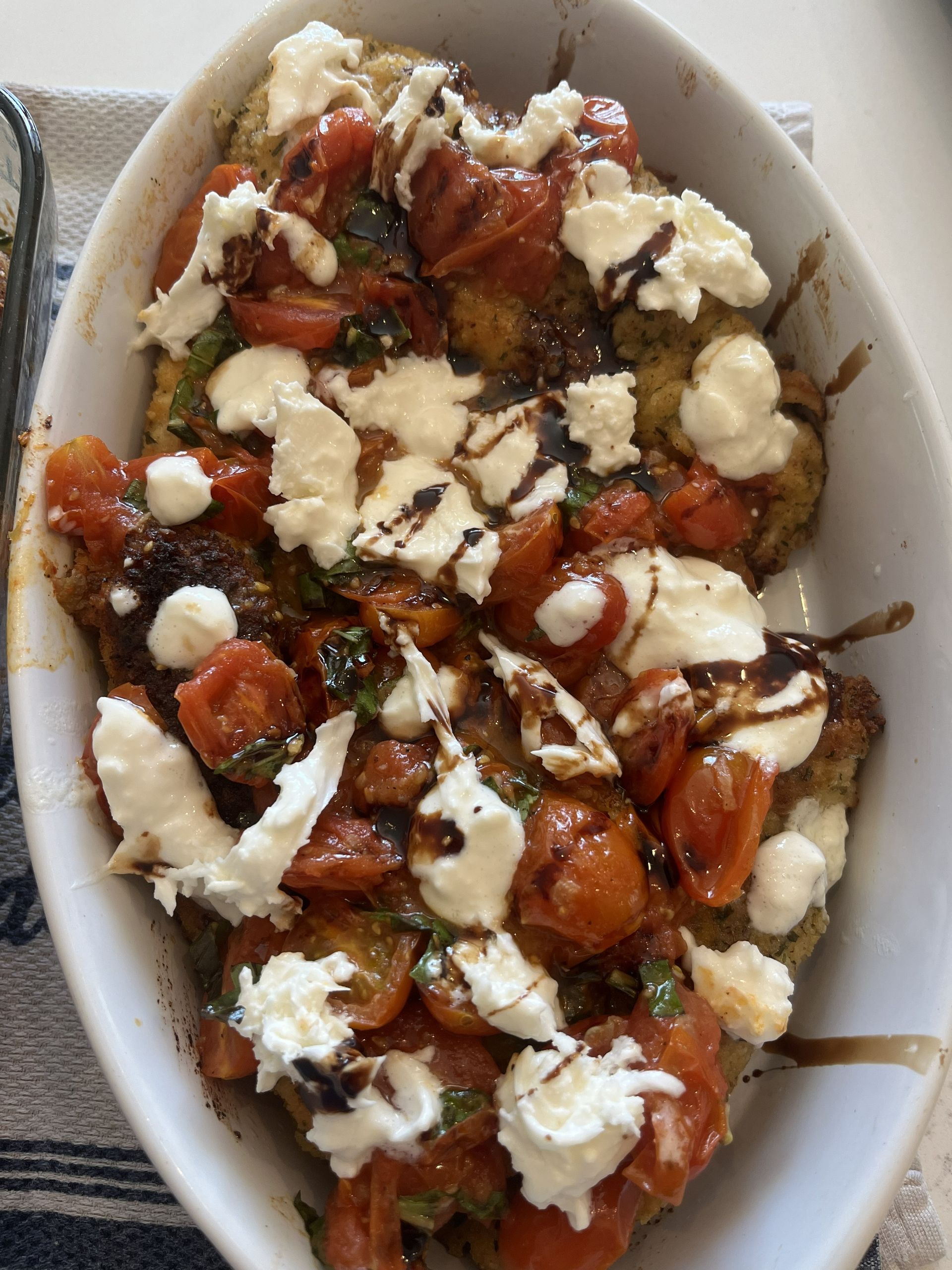 Oval dish of roasted tomatoes and greens topped with crumbled white cheese and balsamic glaze