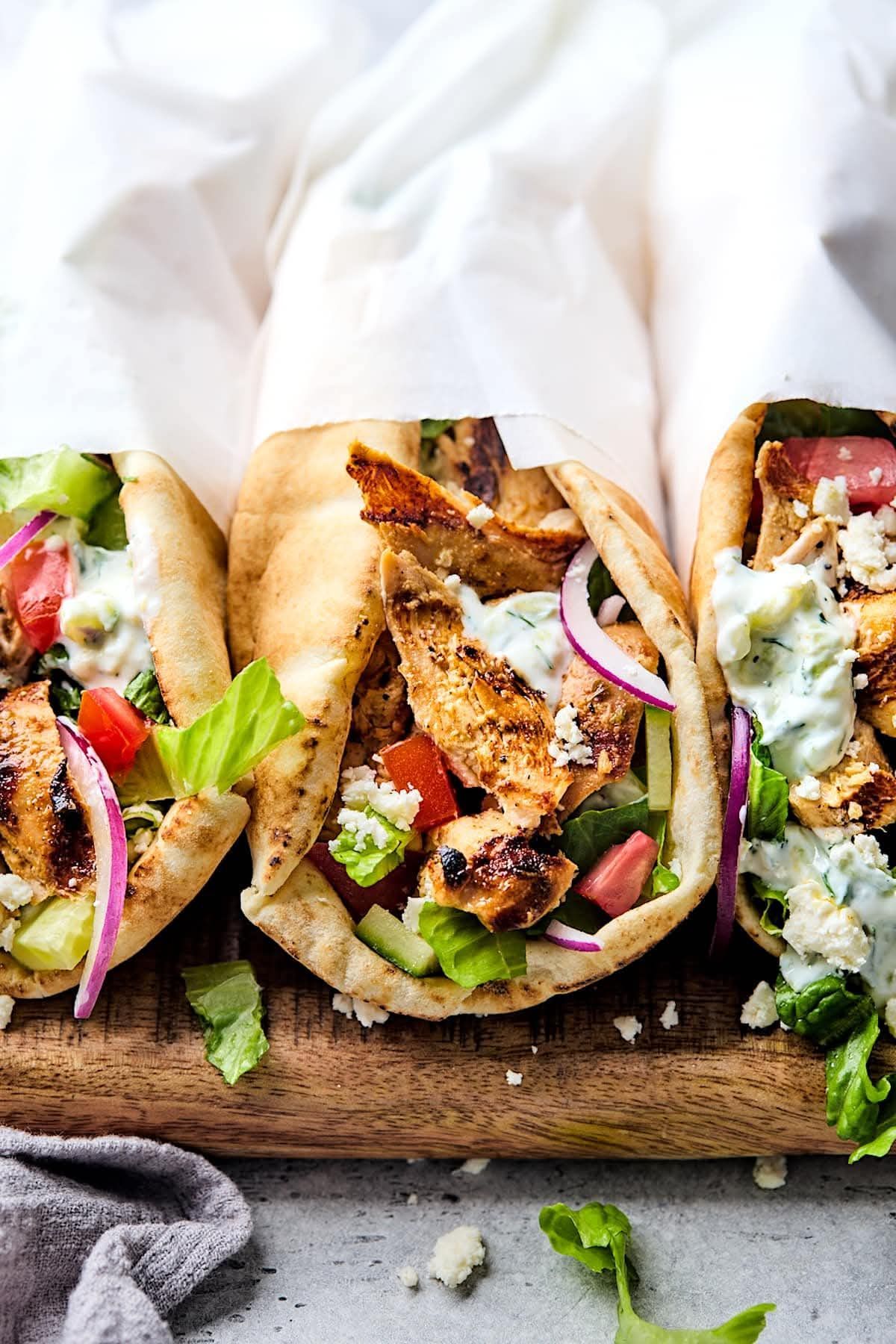 Three grilled chicken tacos with lettuce, onion, and sauce on a wooden board
