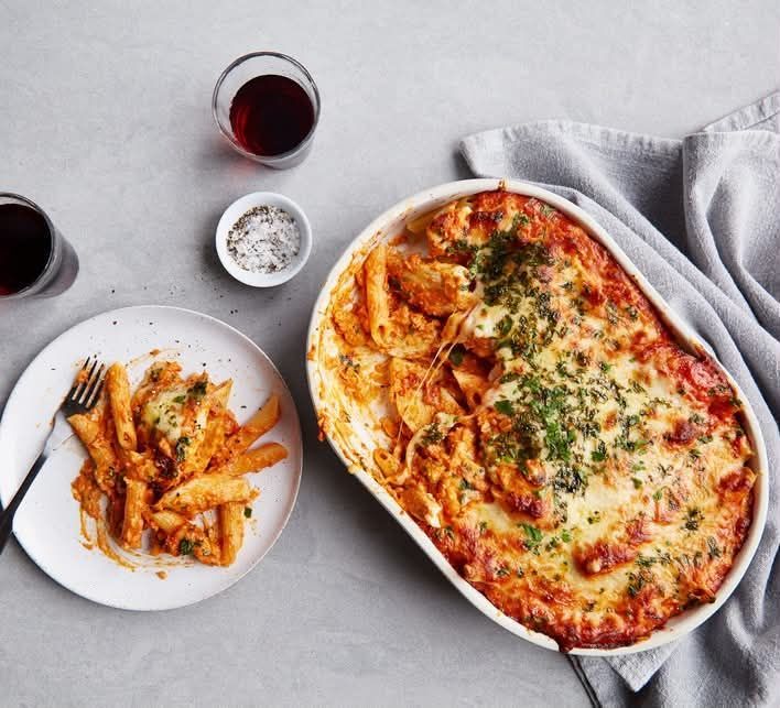 Baked lasagna in a white dish with fries and red wine on a light tablecloth