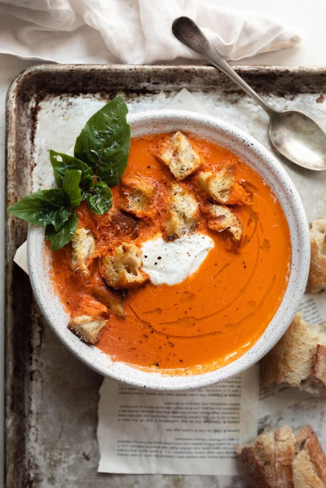 Creamy orange soup topped with croutons and basil in a white bowl on a rustic table