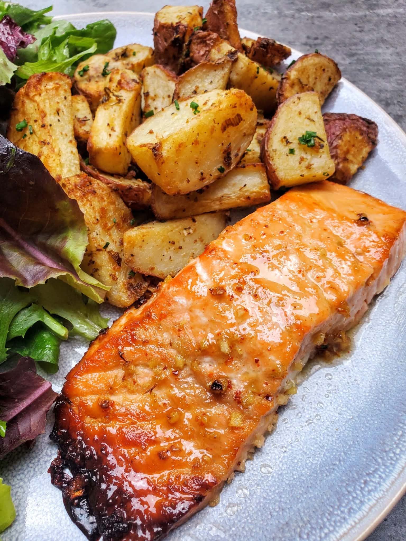 Grilled salmon with roasted potatoes and mixed greens on a white plate
