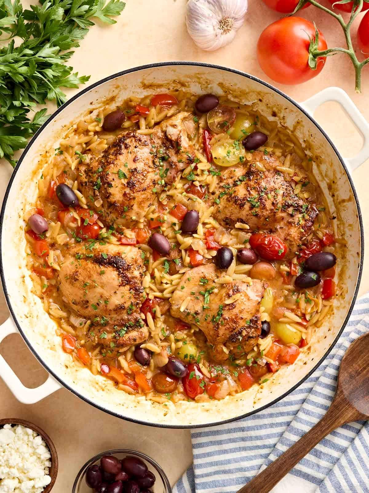 Baked Mediterranean chicken in a skillet with olives, tomatoes, and herbs, served on a table