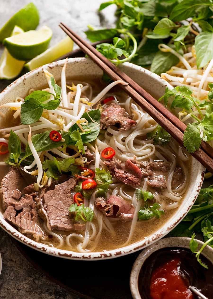 Vietnamese beef pho with noodles, herbs, lime, chopsticks, and chili sauce in a bowl
