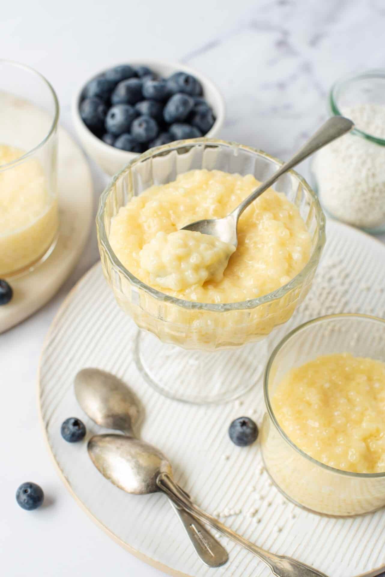 Bowls of creamy yellow dessert topped with berries and spoons on a marble table