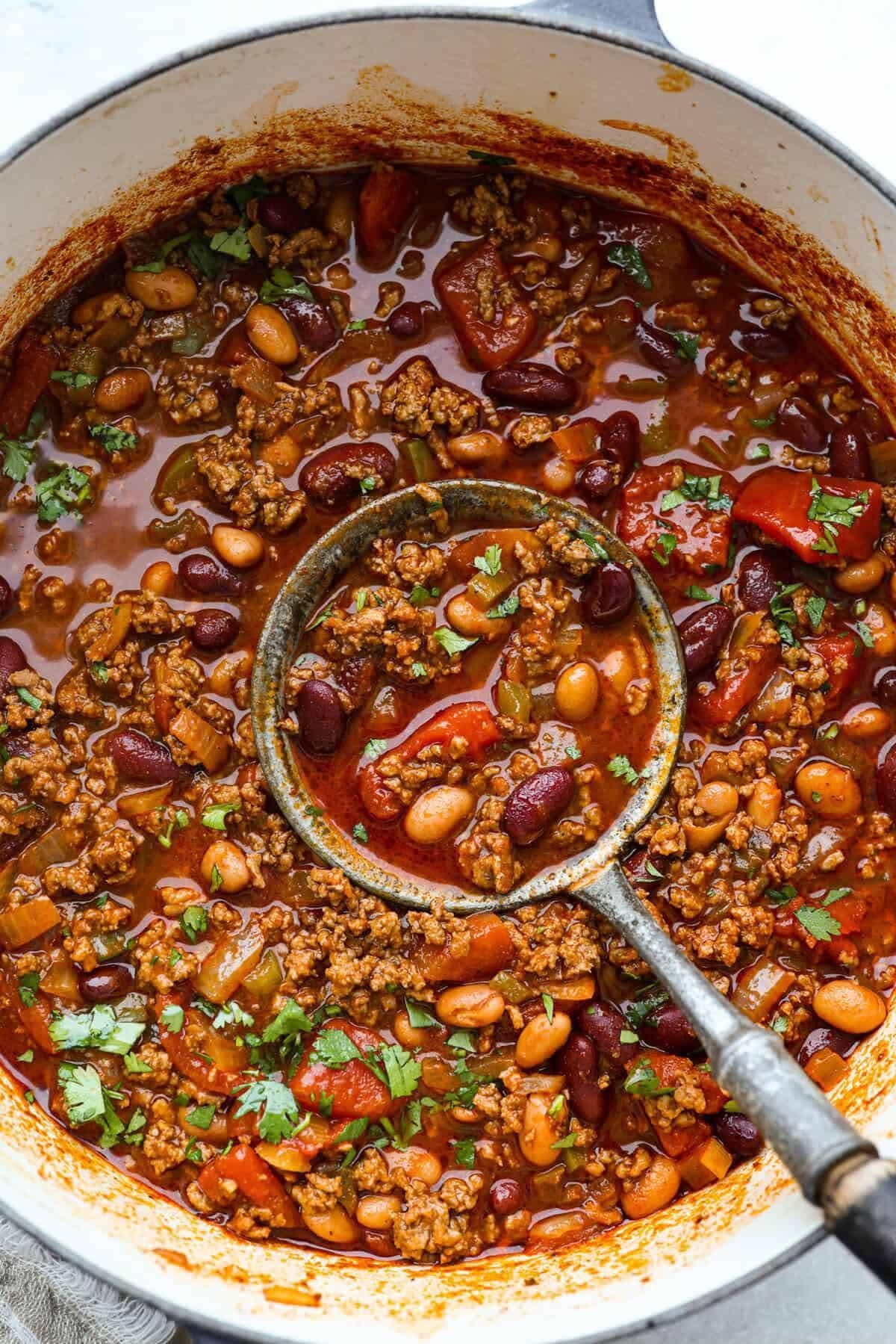 Hearty bean and vegetable stew in a pot, with a ladle stirring the rich red broth.
